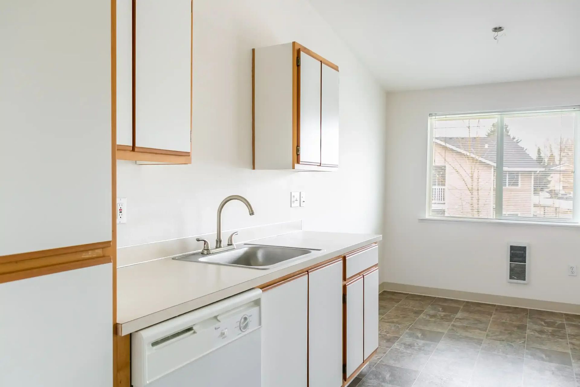 Bright kitchen with white cabinets, sink, dishwasher, and a large window overlooking houses.