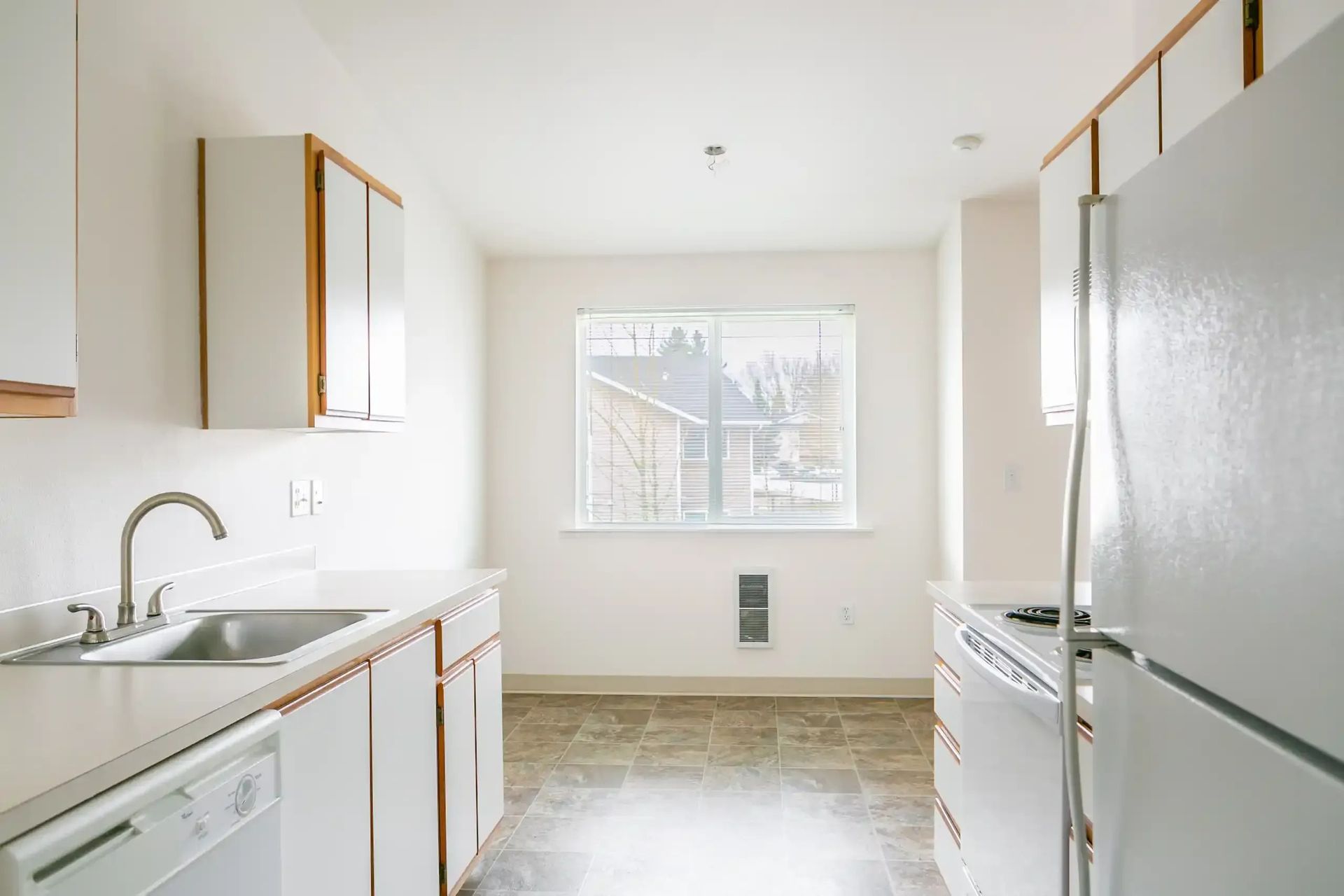 Bright narrow kitchen with white cabinets, appliances, and a window at the far end