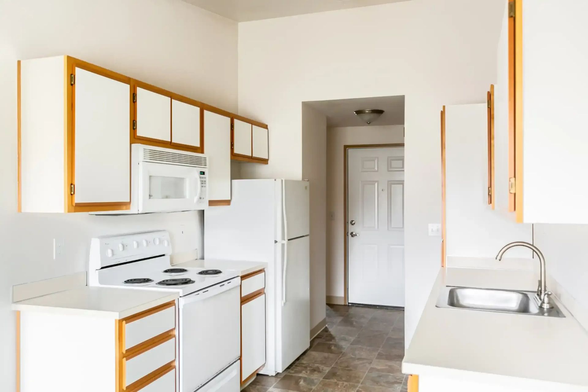 Bright white kitchen with wood-trim cabinets, white appliances, and a sink by the windowless wall.