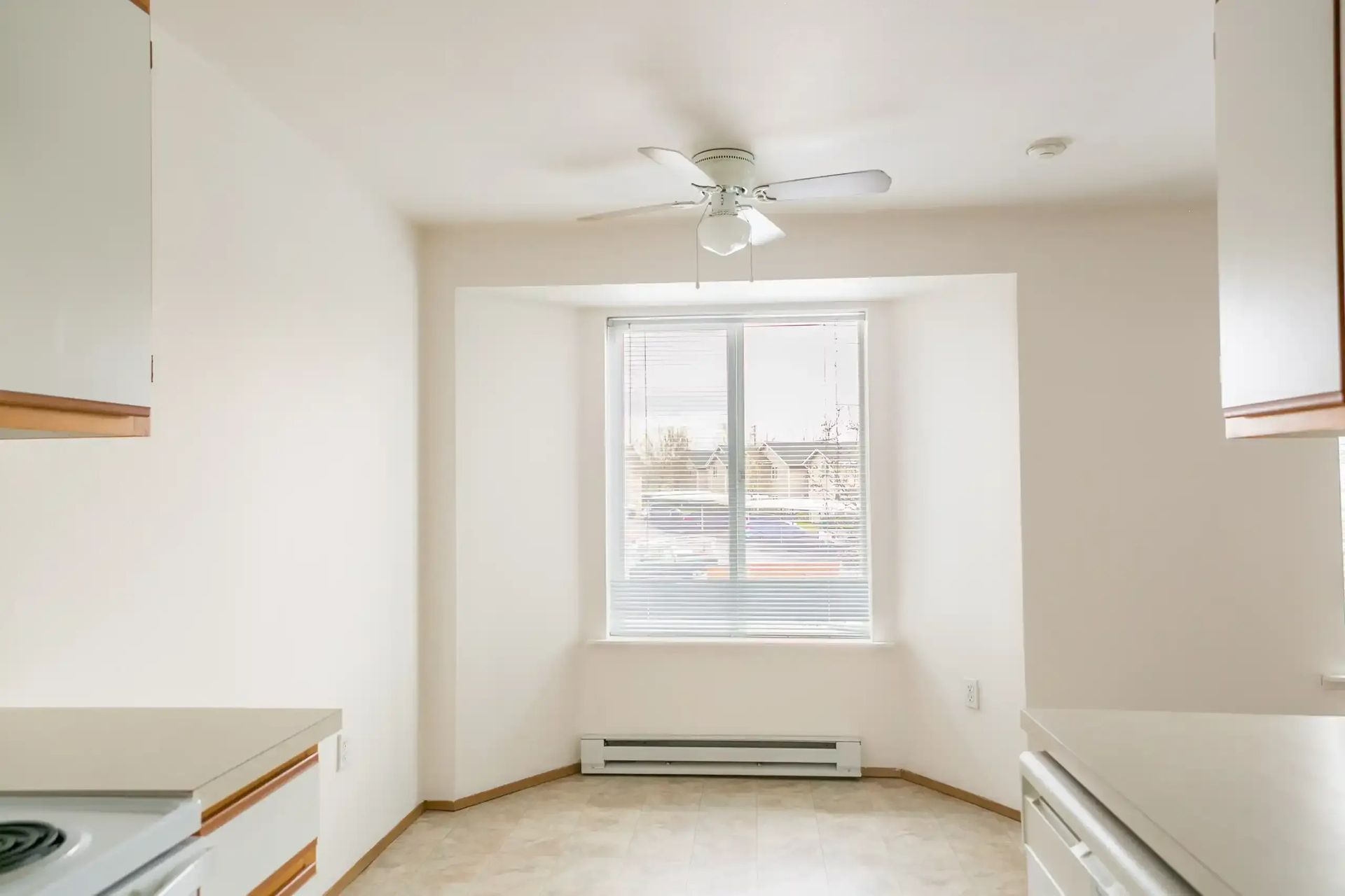 Empty white kitchen with a window, ceiling fan, and built-in cabinets on both sides.