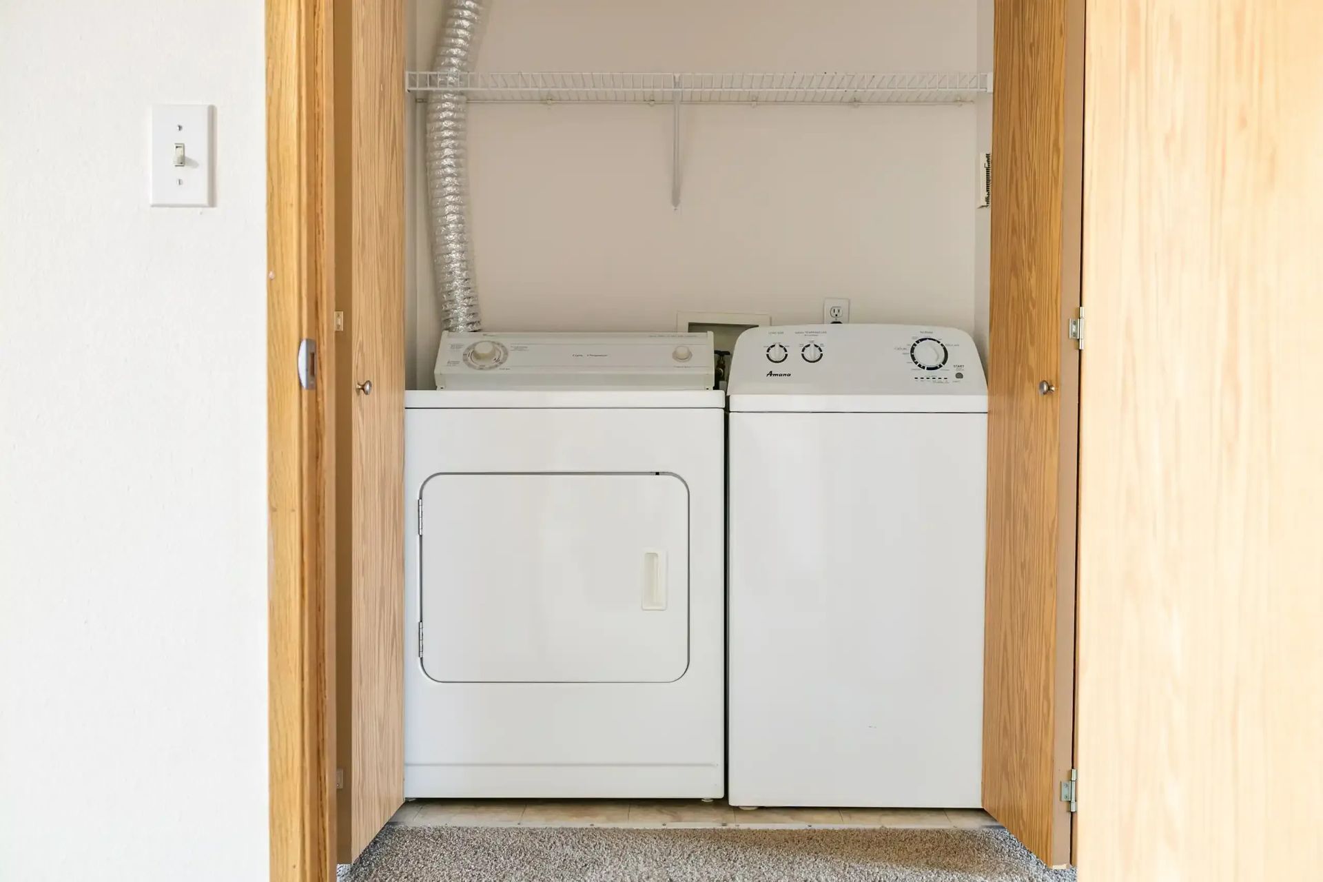 Laundry closet with a white dryer and washer side by side inside a wood-framed alcove
