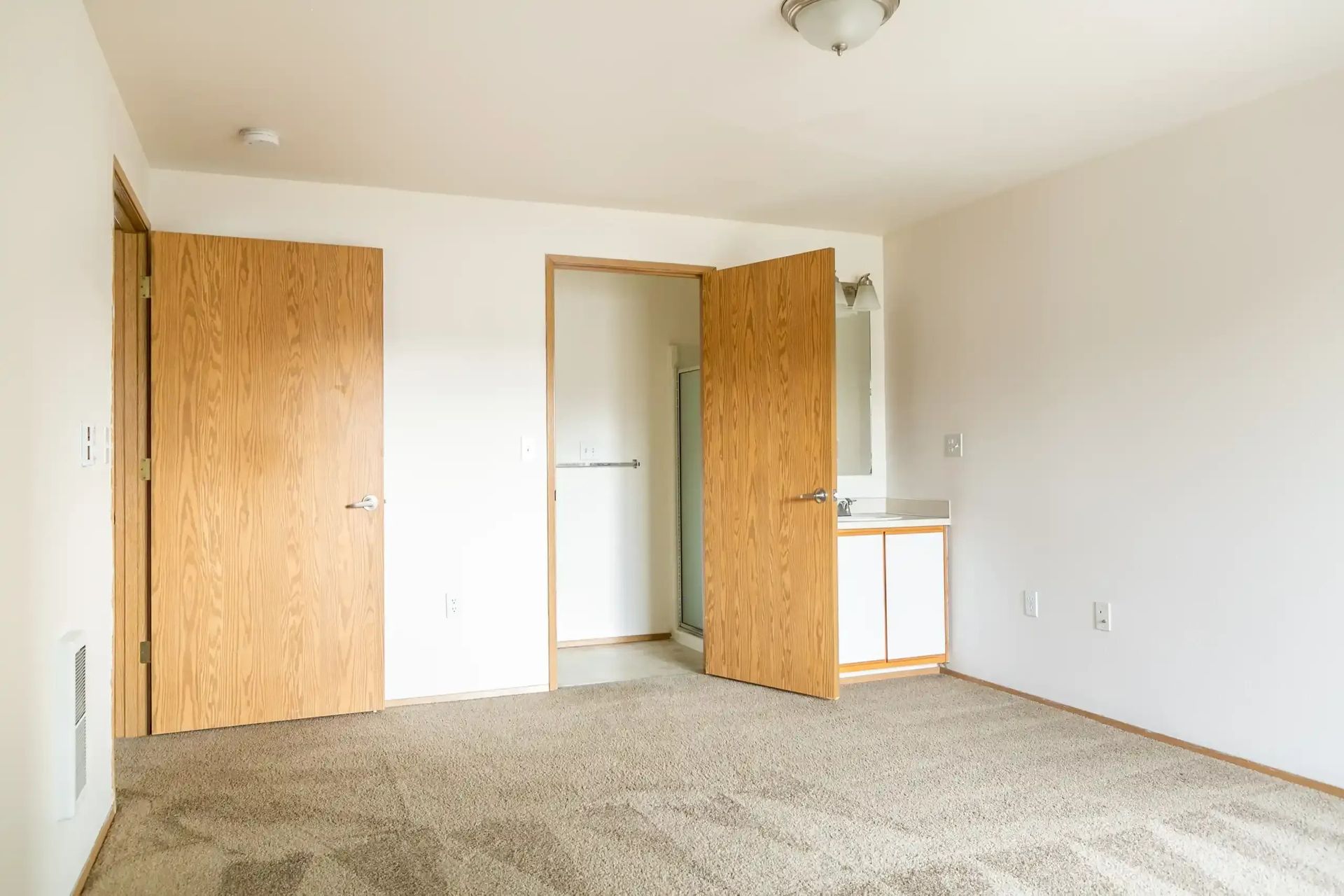 Empty beige bedroom with carpet, two wooden doors, and a small closet area