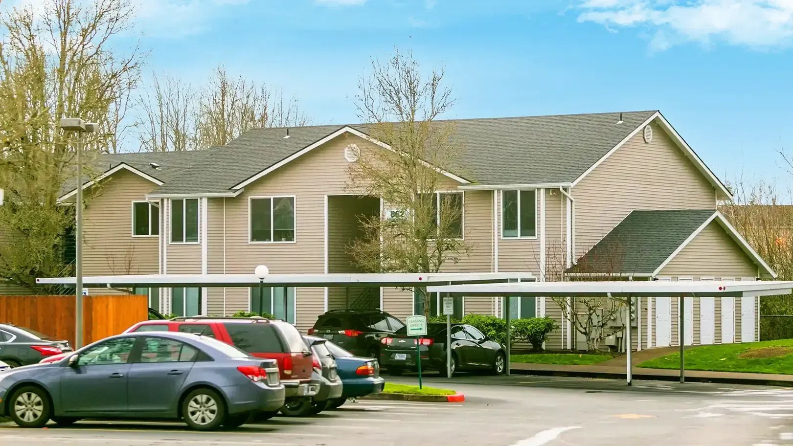 Apartment building with parked cars in front and a covered walkway on a cloudy day