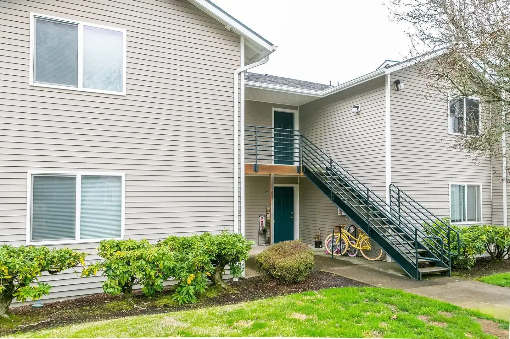 Apartment building exterior with green stairs, beige siding, and a bicycle near the entrance
