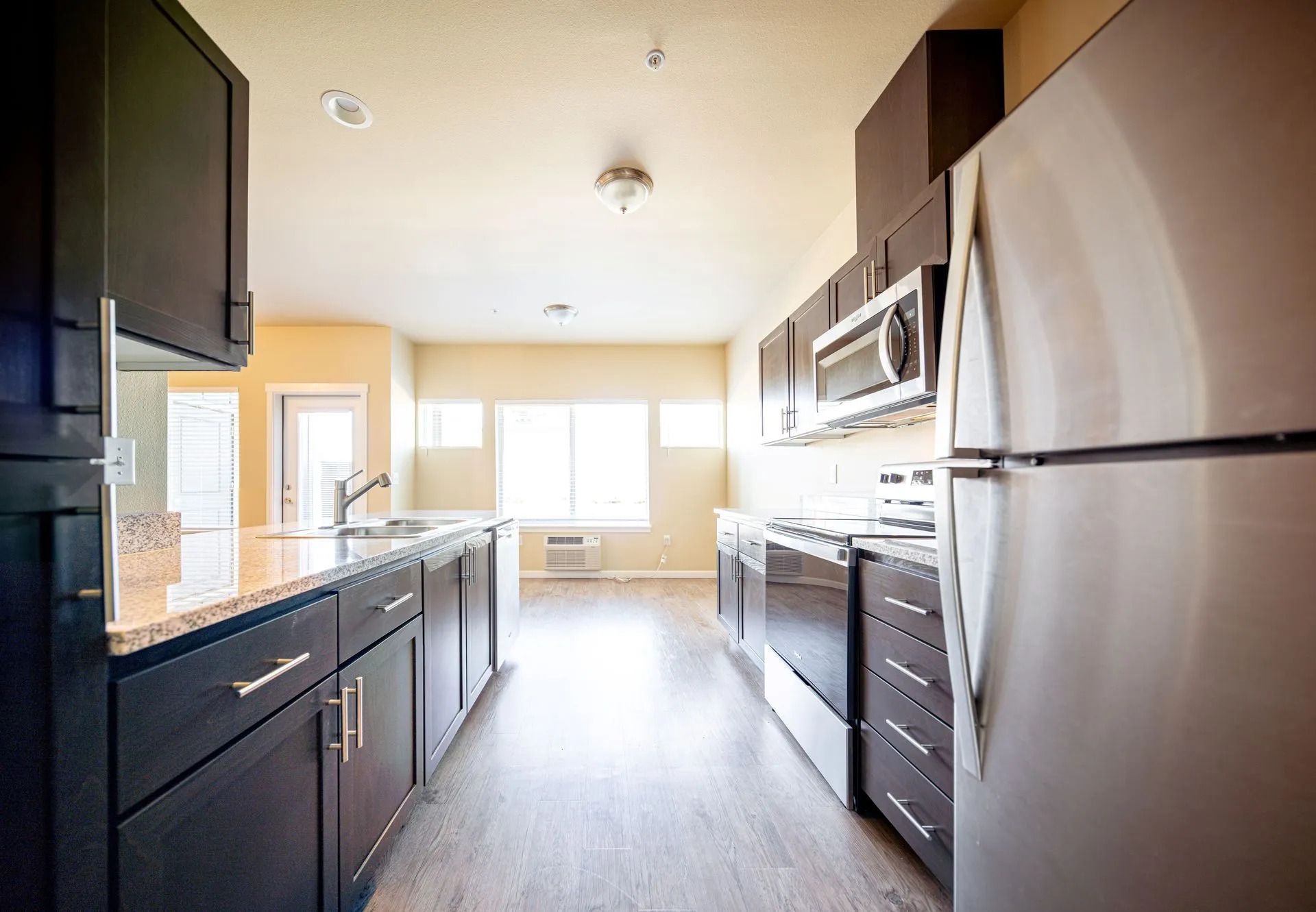 Modern kitchen with dark cabinets, stainless steel appliances, and bright windows at the end of the room