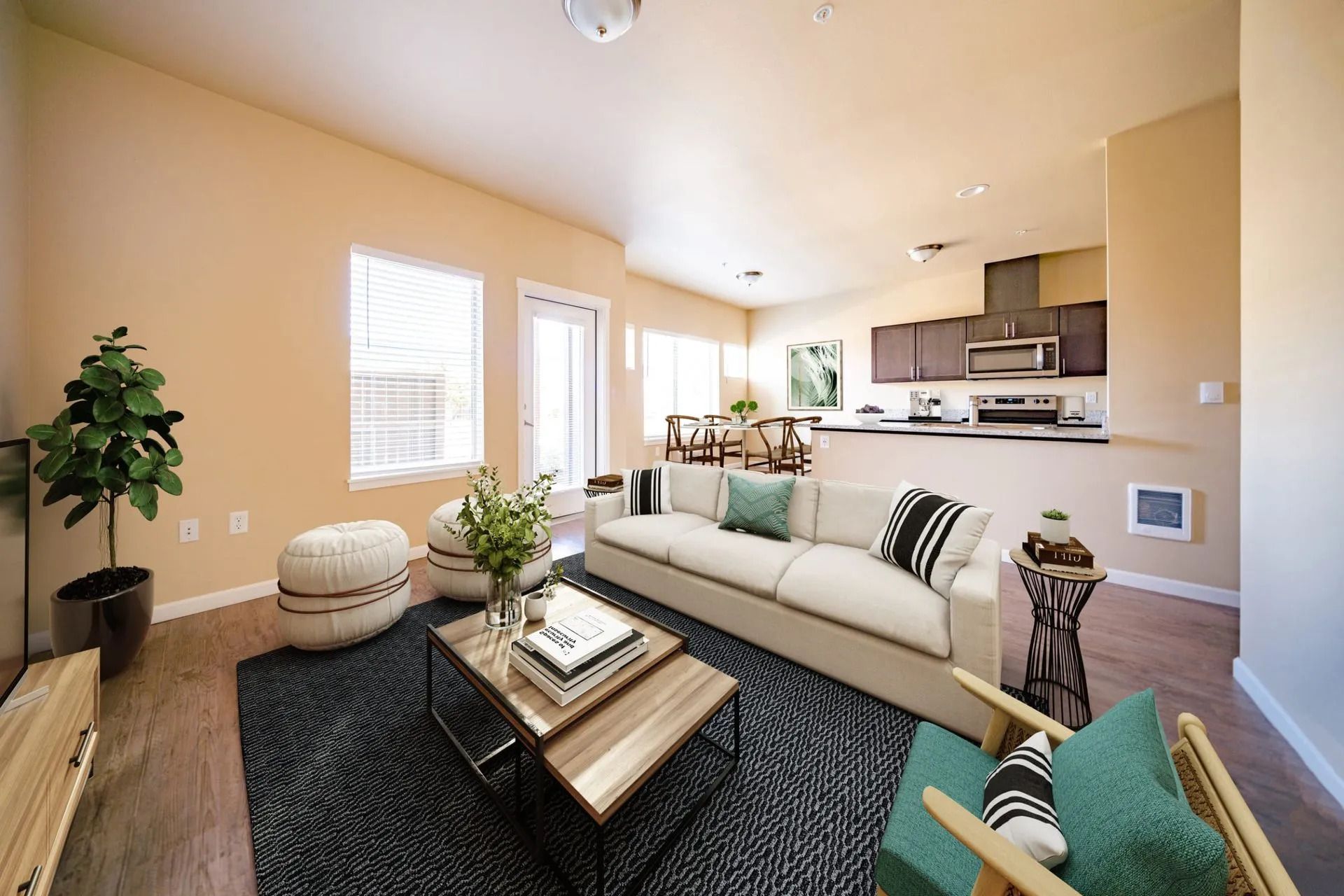 Bright modern living room with beige sectional, black rug, wood coffee table, and open kitchen beyond.