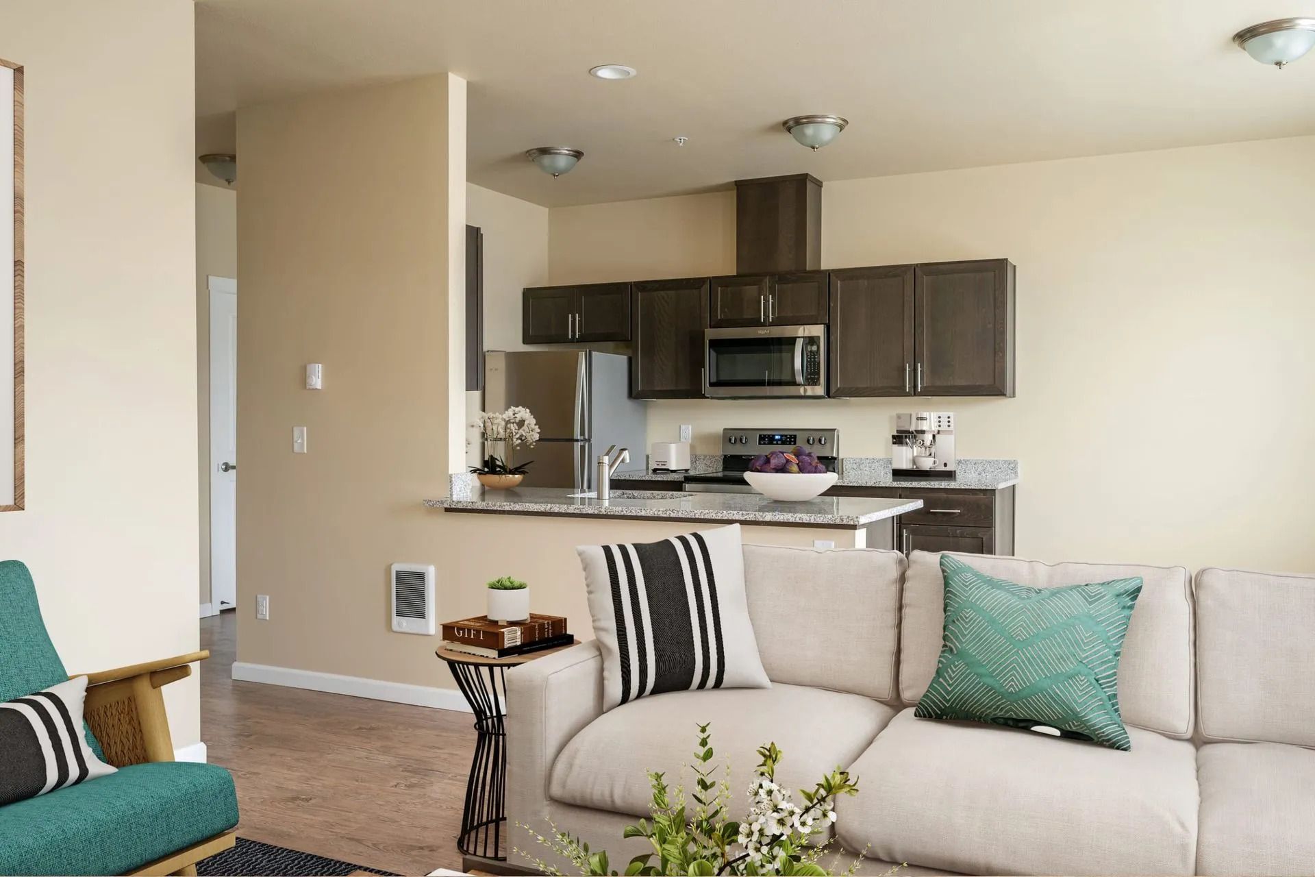 Living room with beige sofa, teal chair, and open kitchen in the background