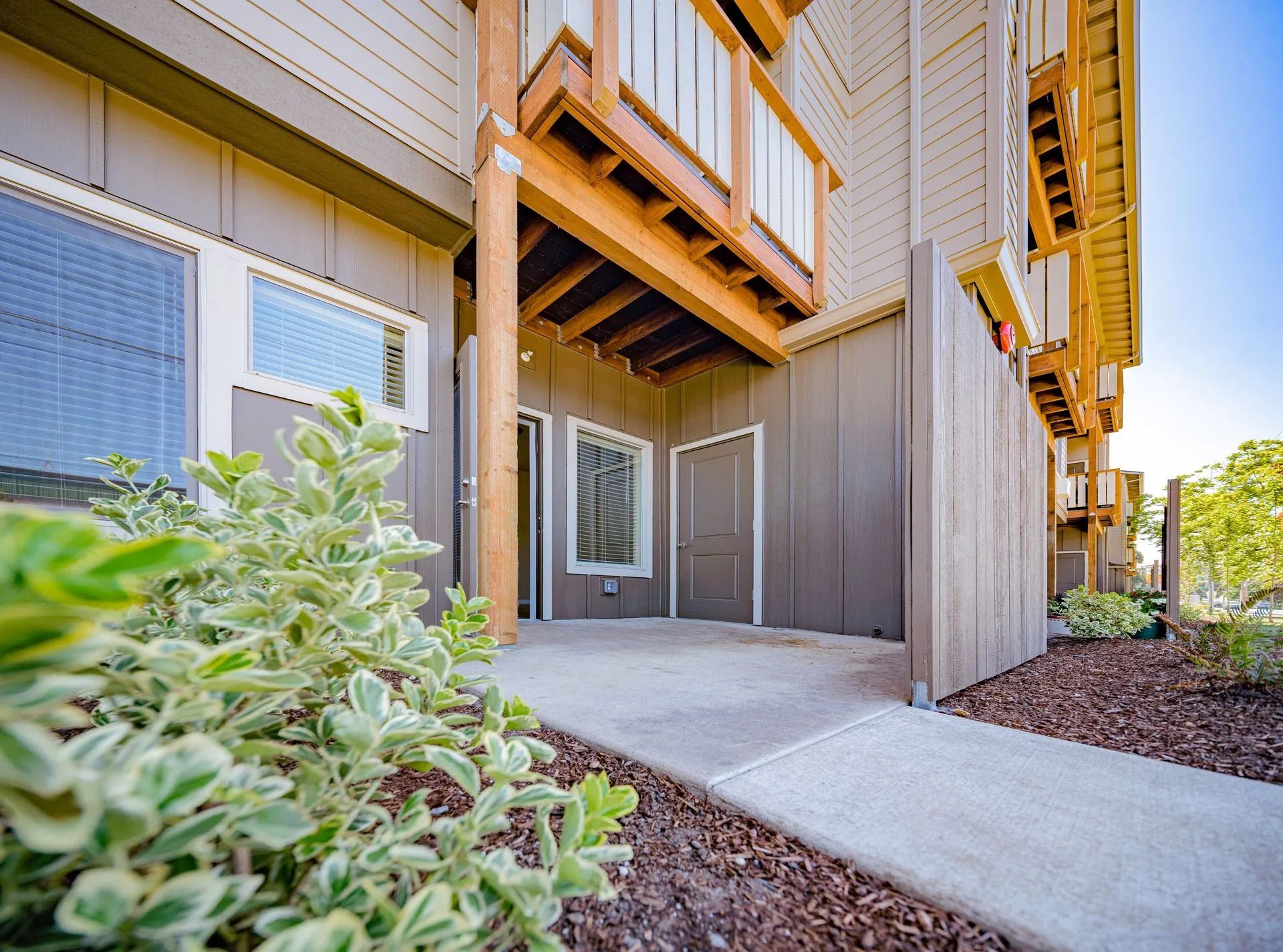 Apartment entrance with concrete walkway, brown siding, and potted greenery at a ground-level patio.