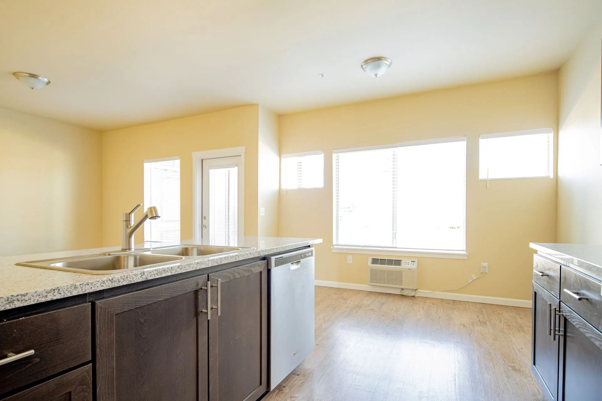 Bright empty kitchen with dark cabinets, granite island, and large sunlit windows.