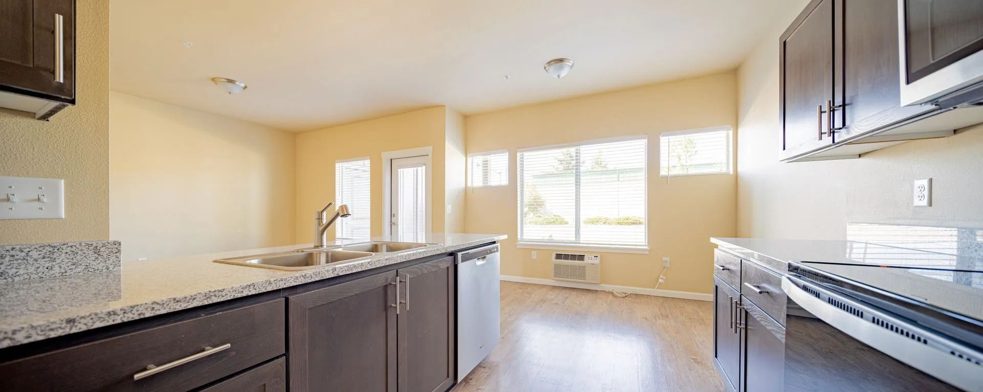 Bright kitchen with dark cabinets, granite counters, stainless appliances, and large windows