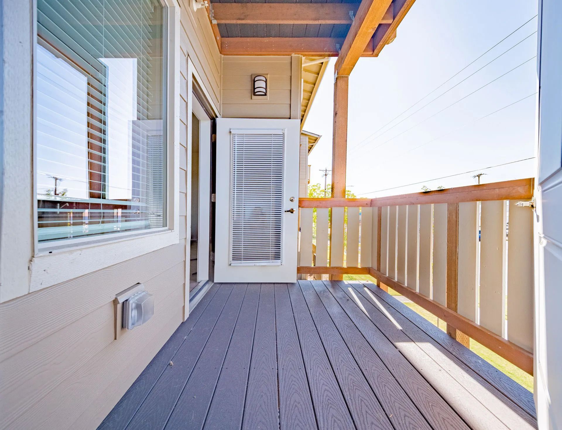 Covered wooden balcony with white siding, railing, and sliding door in bright sunlight