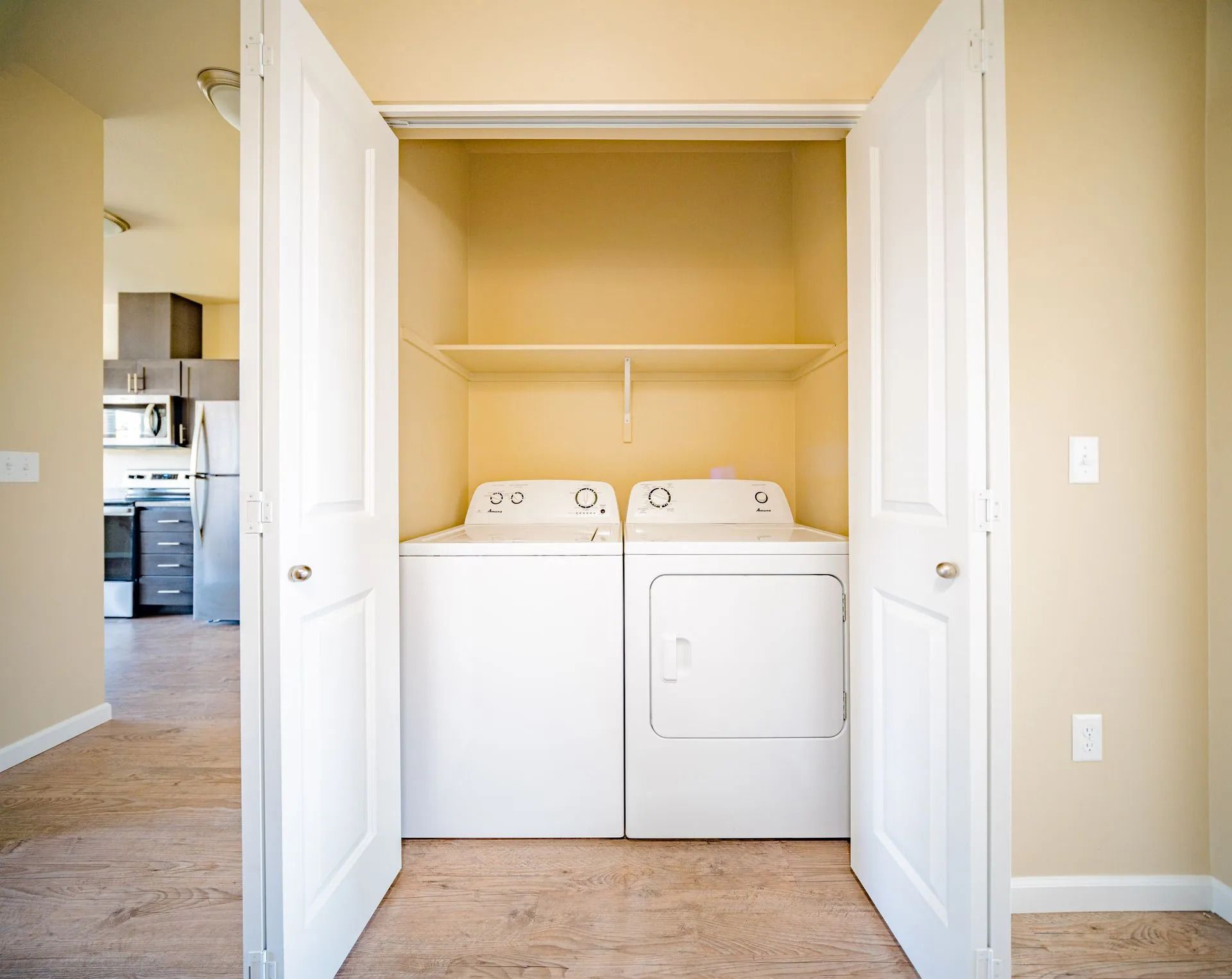 Laundry closet with white washer and dryer behind open double doors in a beige hallway