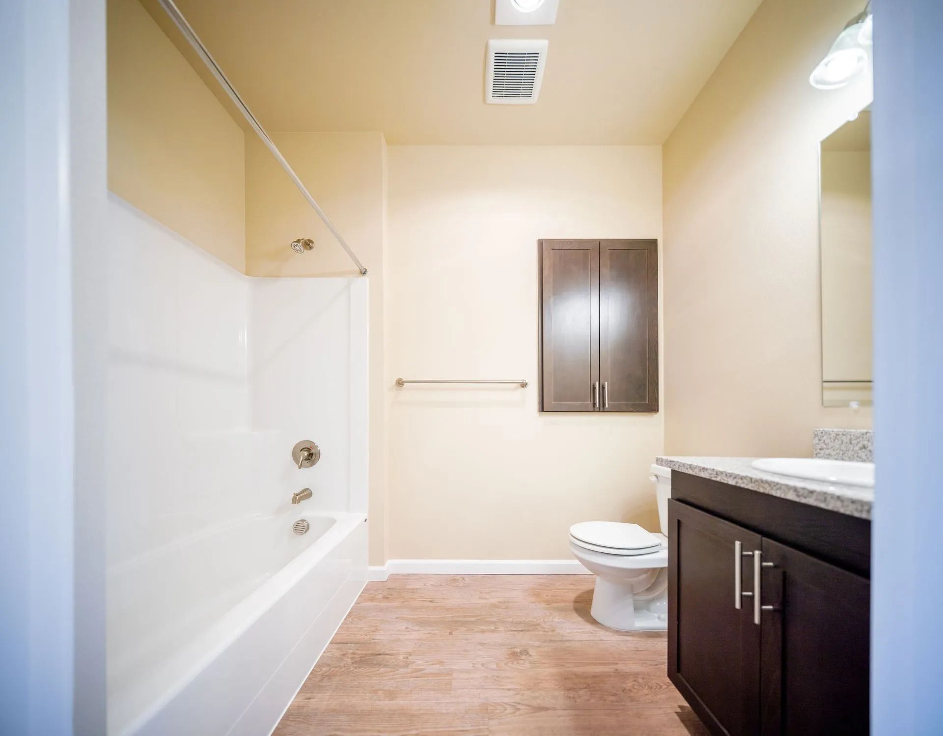 Bright bathroom with bathtub, toilet, dark vanity, and beige walls