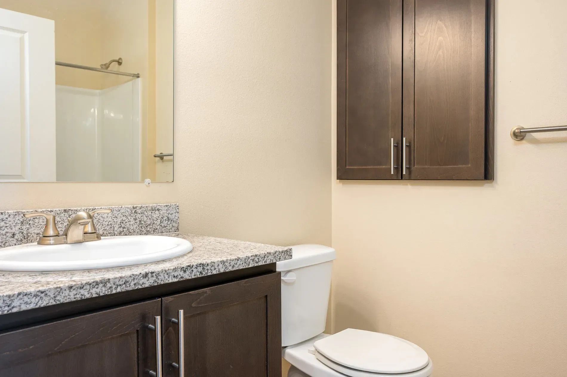 Bathroom vanity with granite countertop, sink, mirror, toilet, and dark wood cabinets.