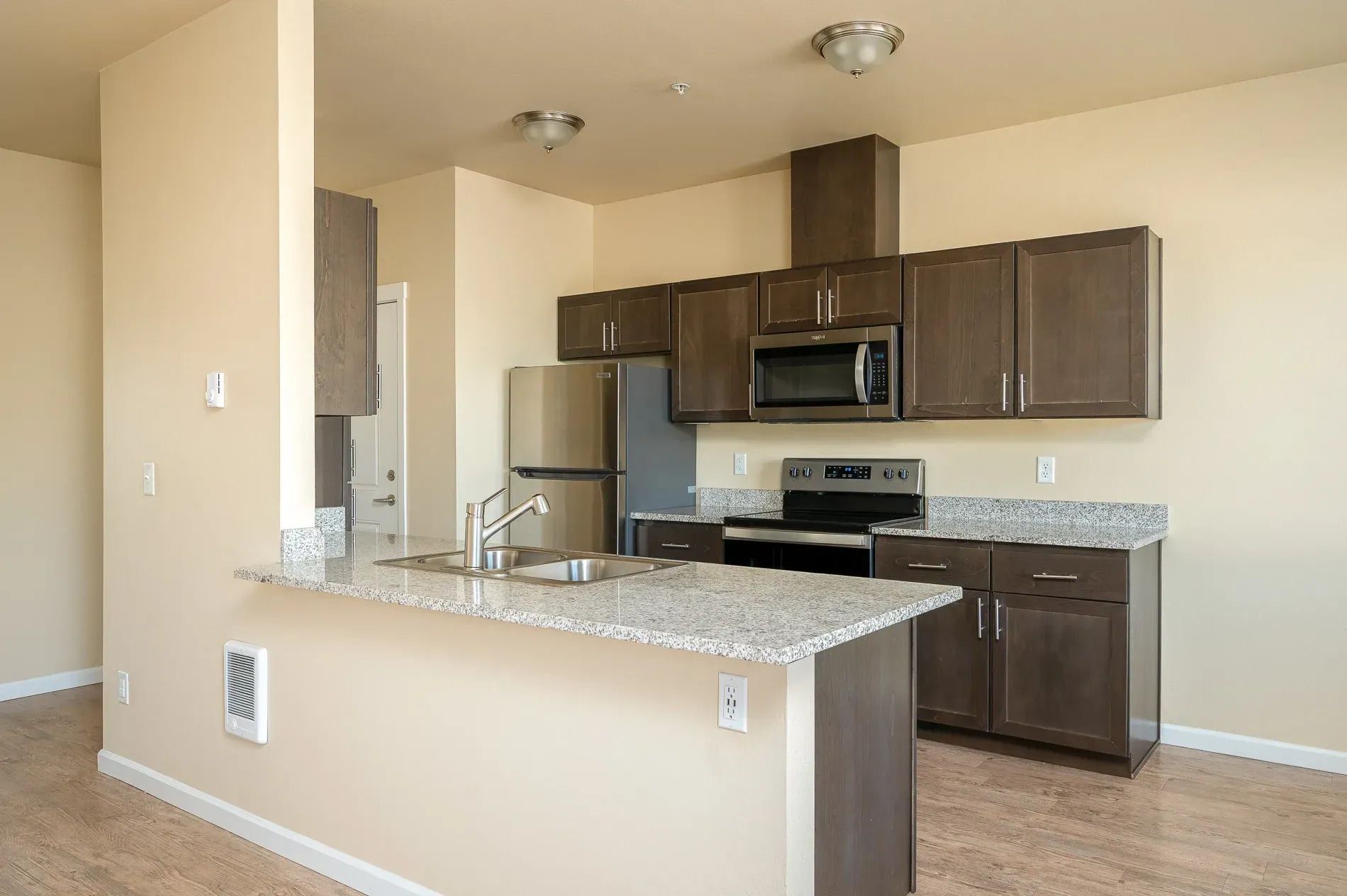 Empty modern kitchen with dark cabinets, stainless steel appliances, and a granite breakfast bar.