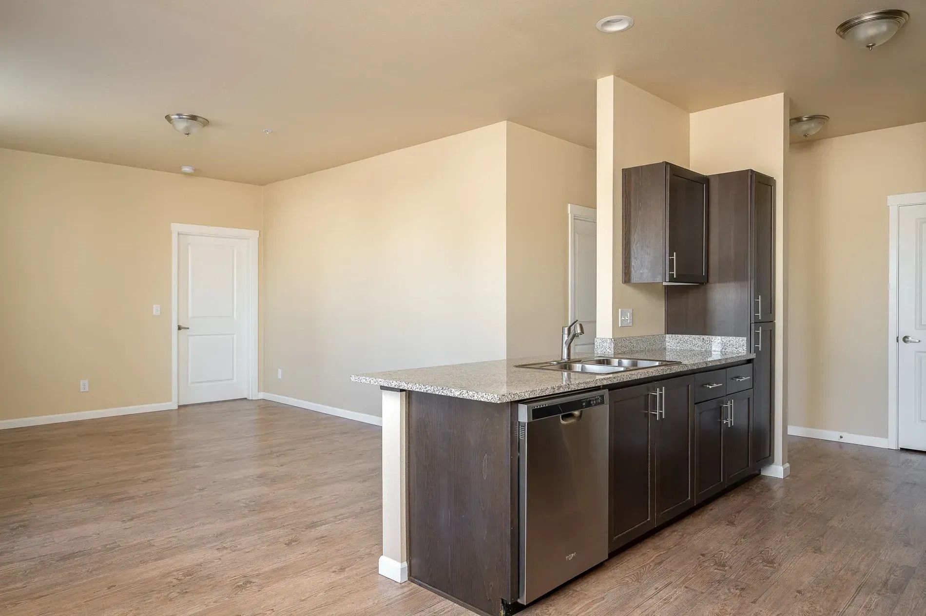 Empty apartment kitchen with dark cabinets, granite island, and beige walls