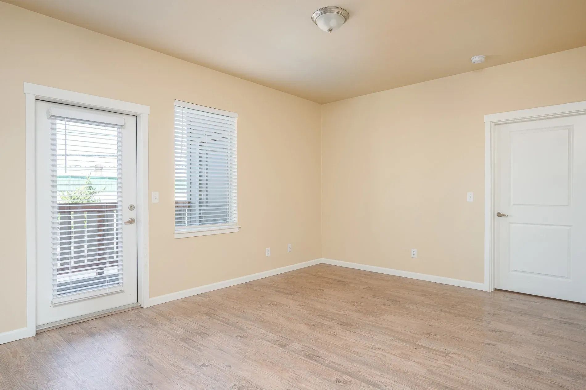 Empty beige room with carpet, two windows, and a white door