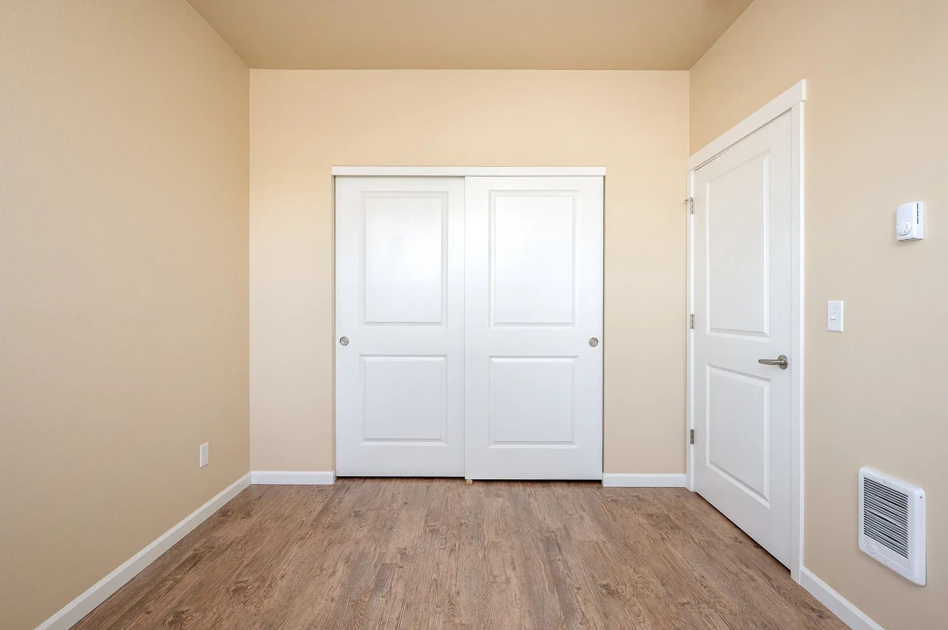 Empty beige bedroom with closet doors, a side door, and carpeted floor.
