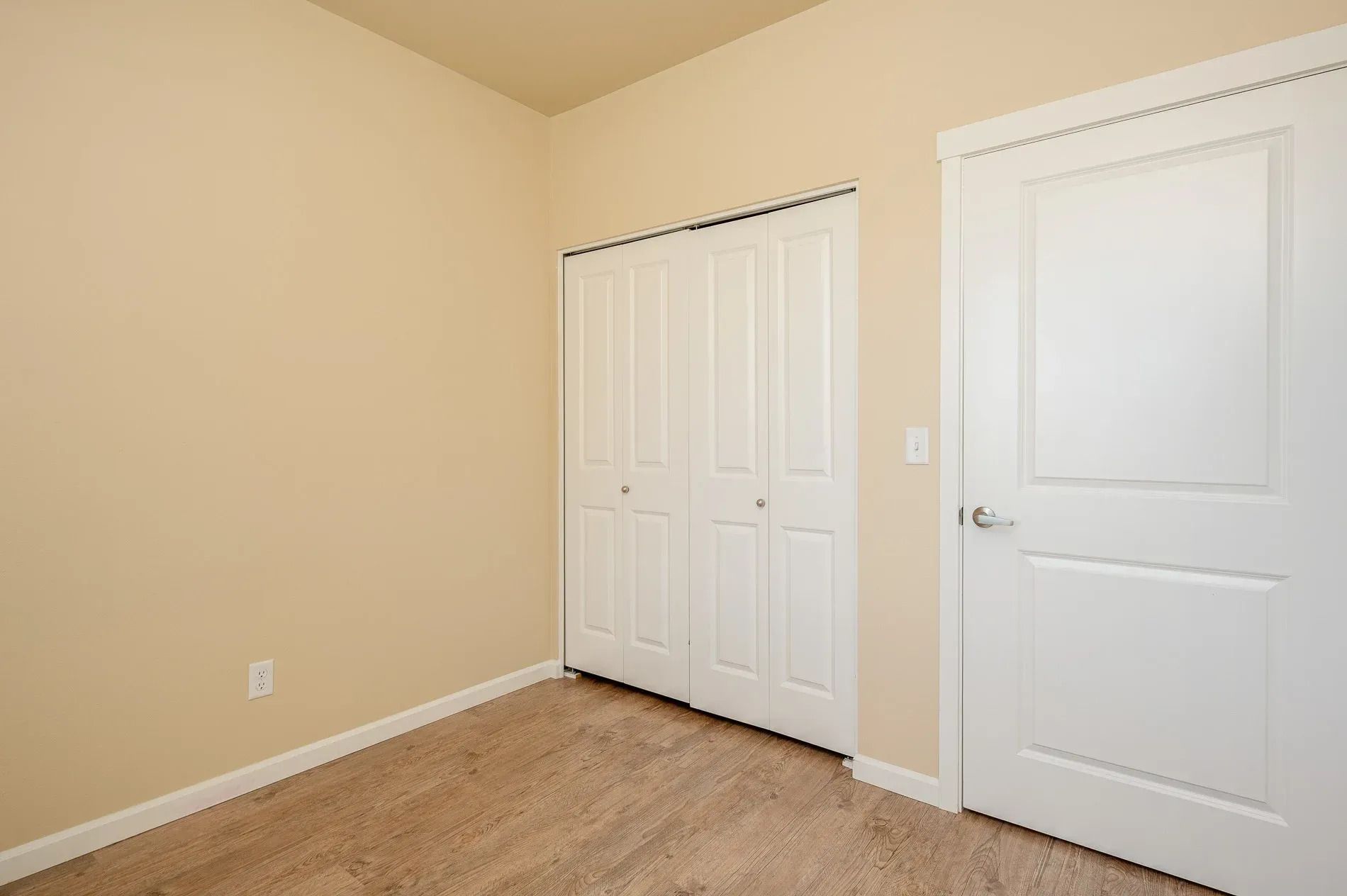 Empty beige bedroom with carpet, double closet doors, and a white door.