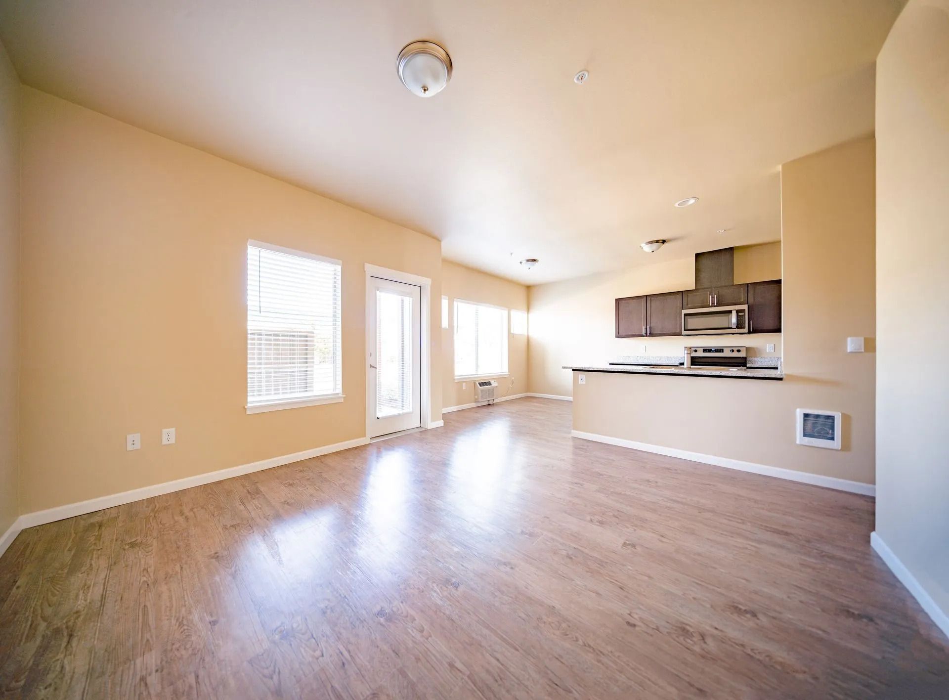 Empty beige open-plan living room with wood floors and a compact kitchen area