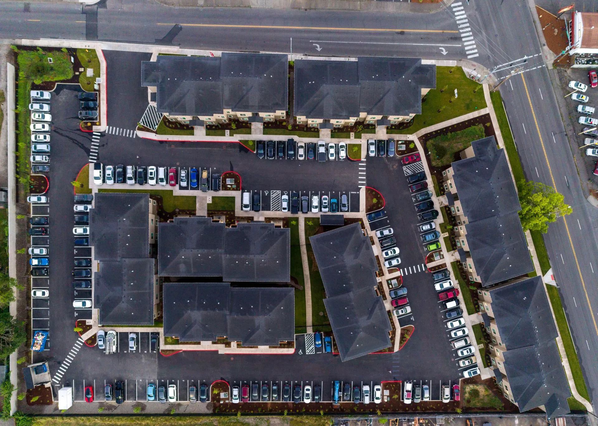 Aerial view of a large parking lot and commercial building complex beside a road.