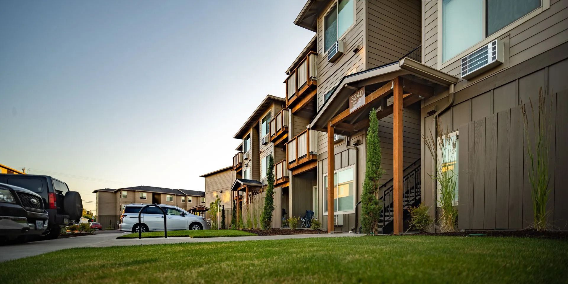 Row of modern townhouses with parked cars along a quiet suburban street at sunset
