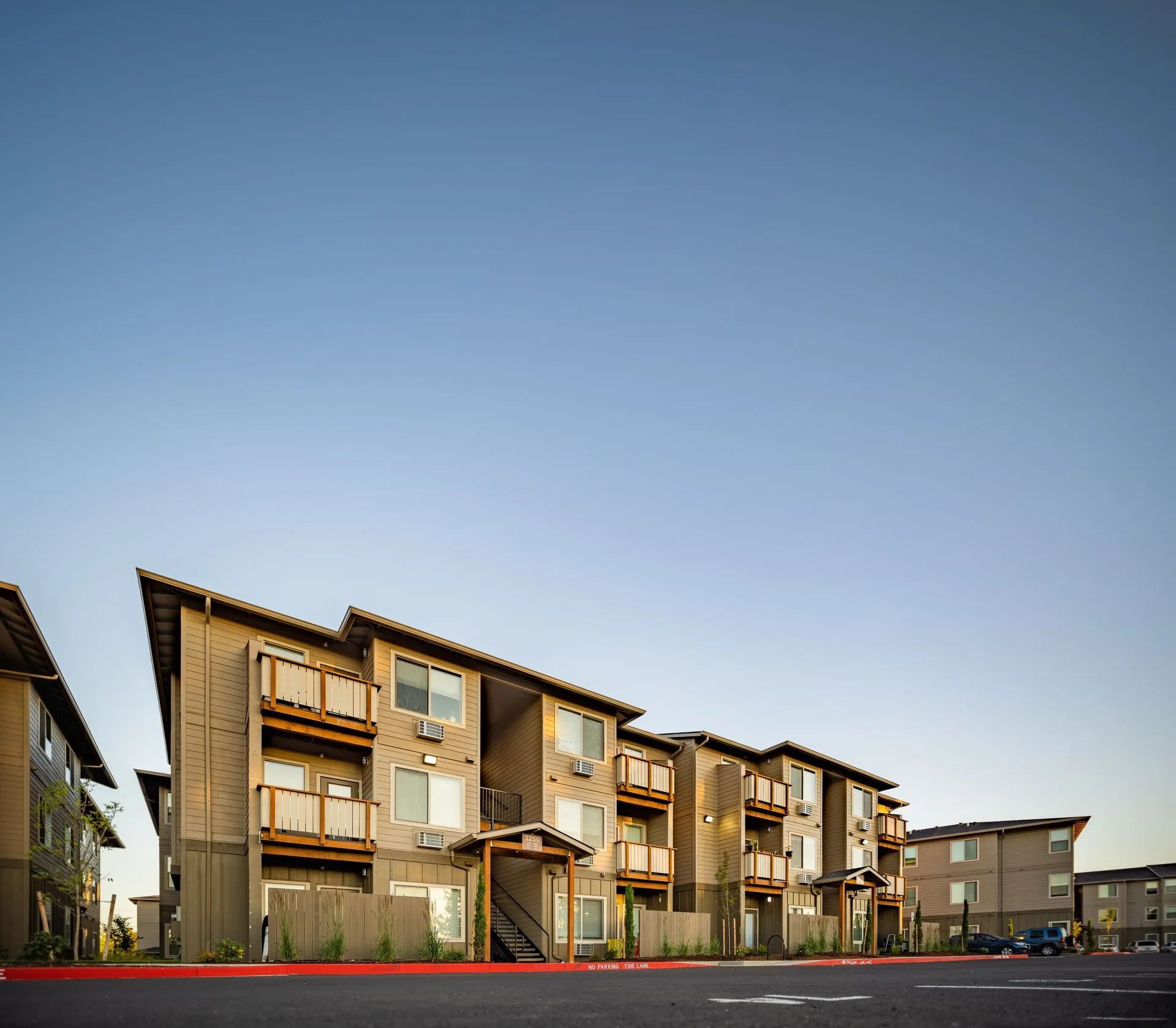 Modern apartment buildings under a clear blue sky, with balconies and a paved parking area in front