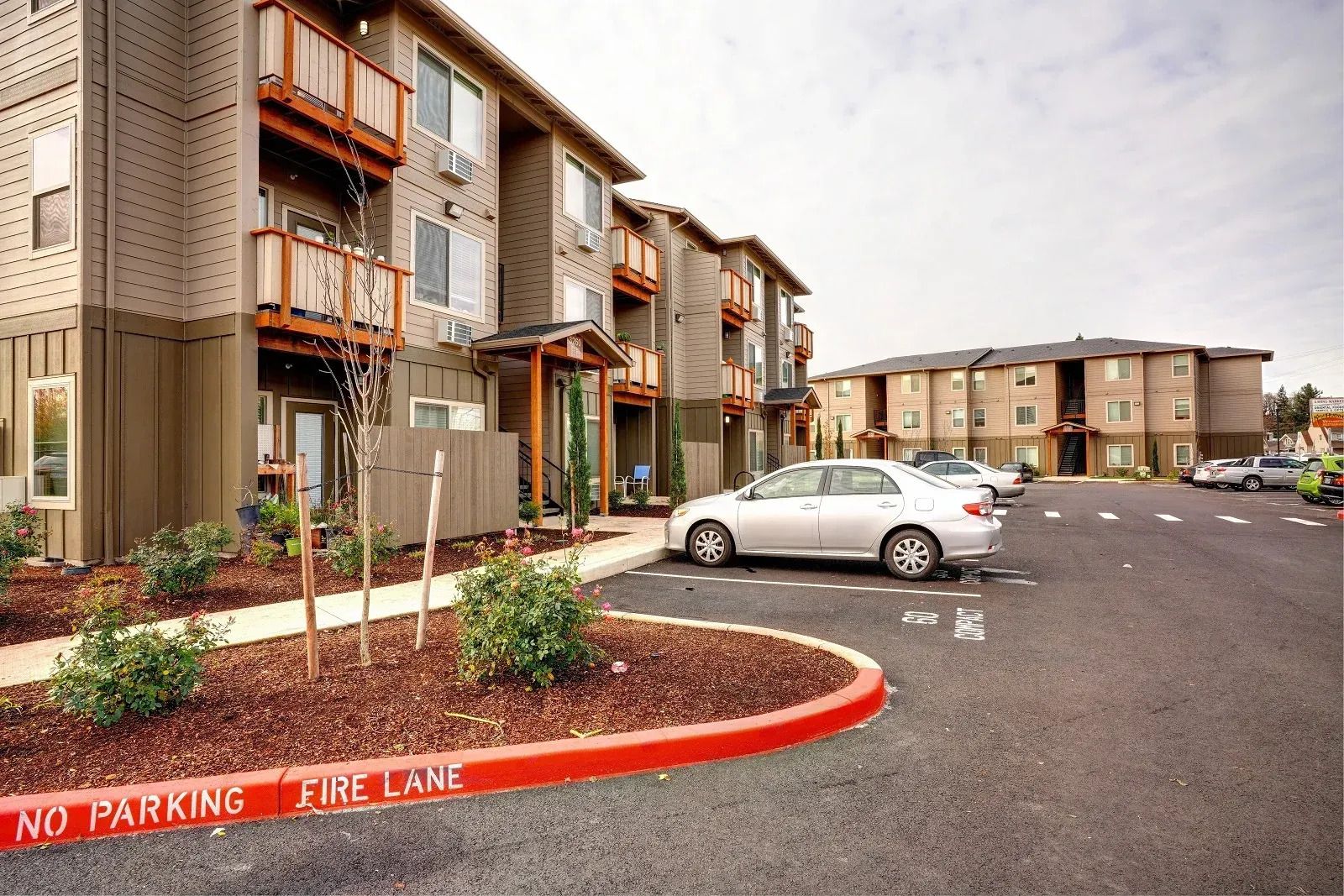 Apartment complex parking lot with a white car and a red curb marked “No Parking Fire Lane”