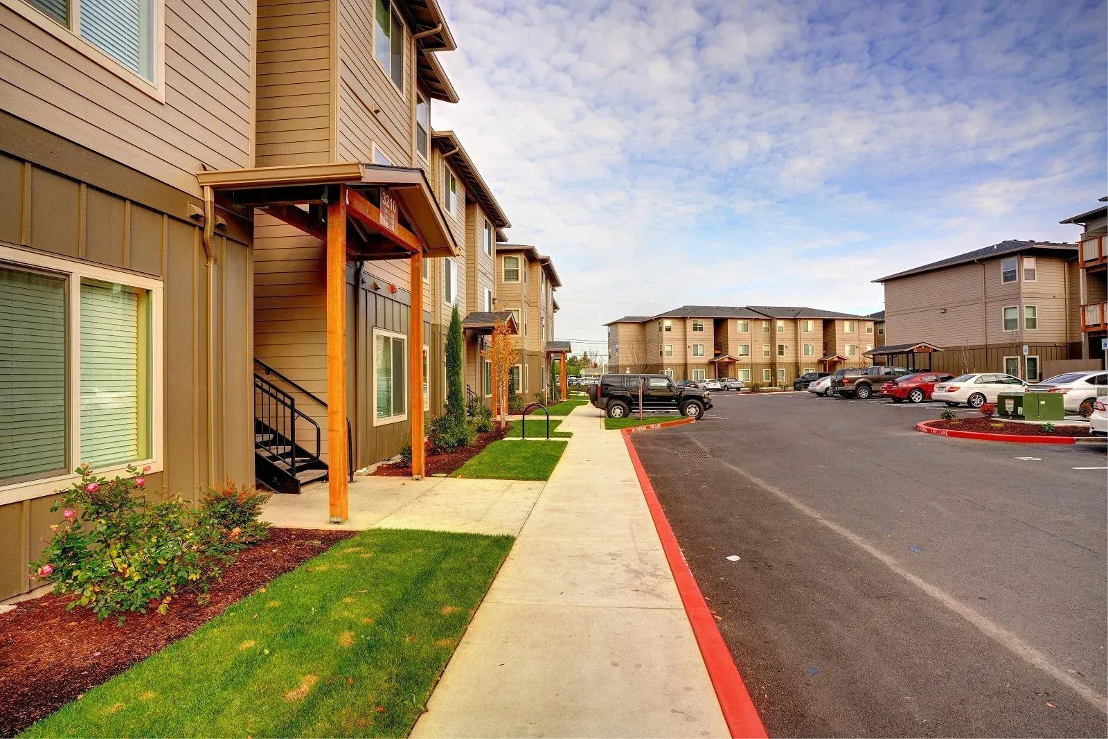 Apartment complex walkway beside parked cars on a sunny day