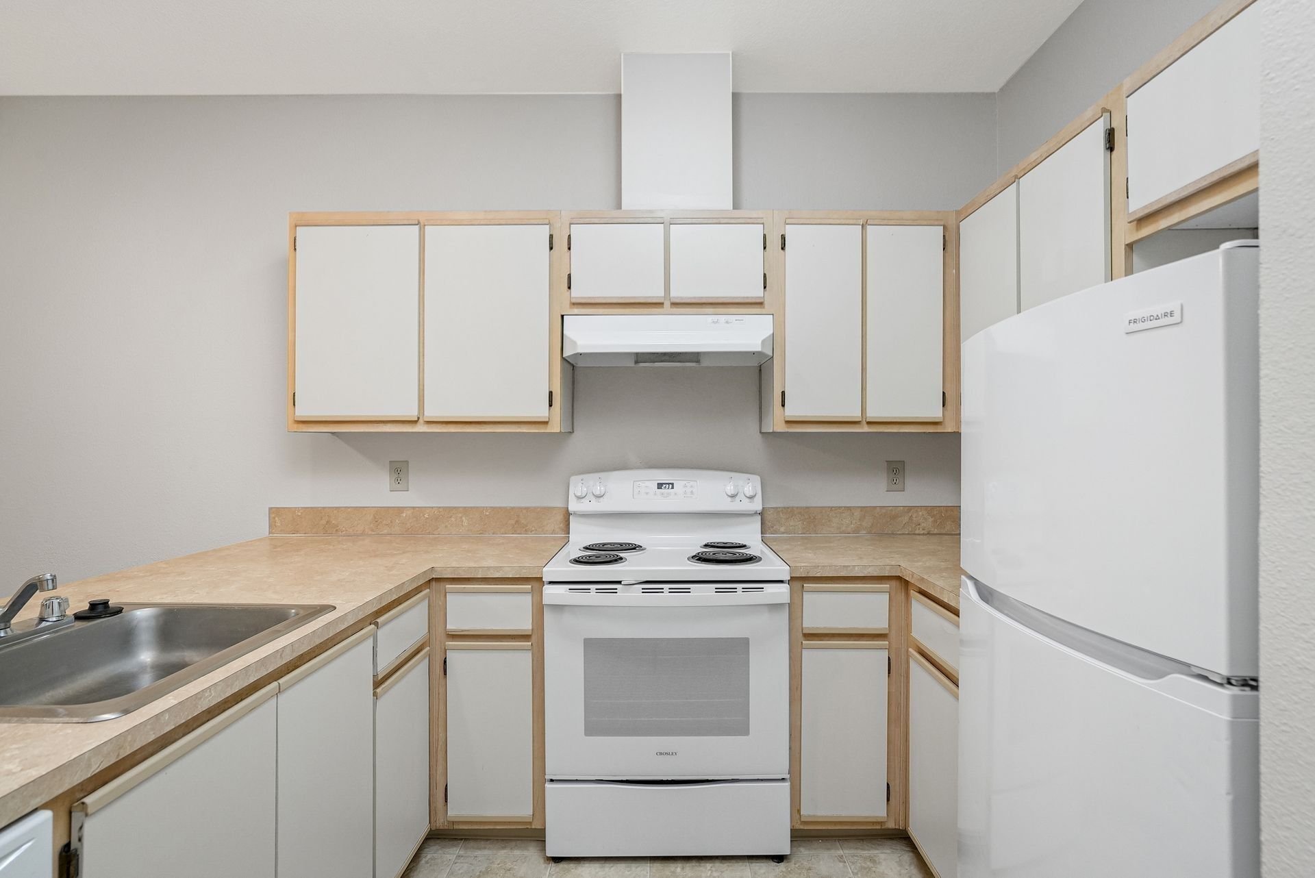 Small kitchen with white appliances, light wood cabinets, and beige countertops.