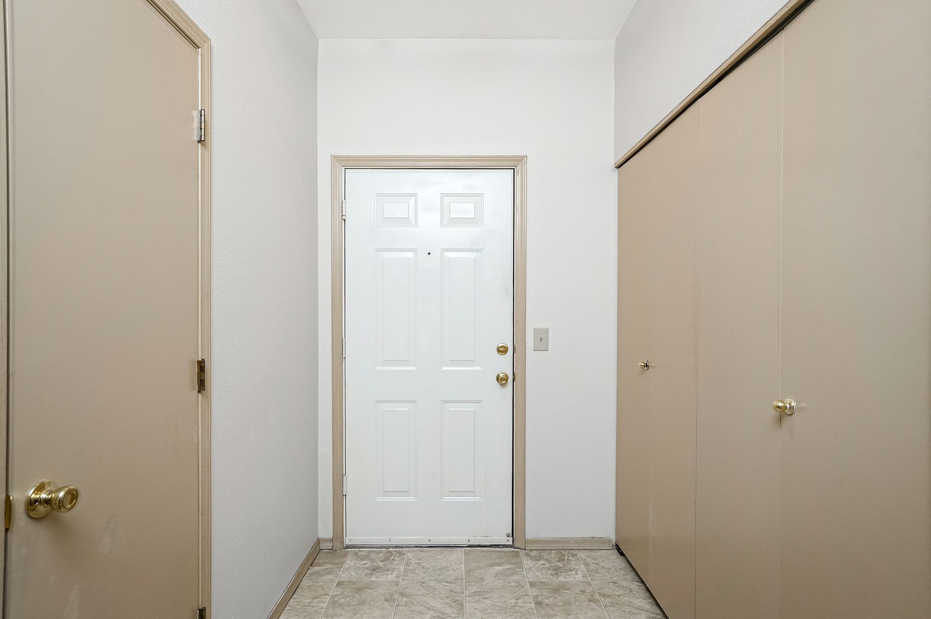 Narrow hallway with white front door, beige walls, and closet doors on both sides