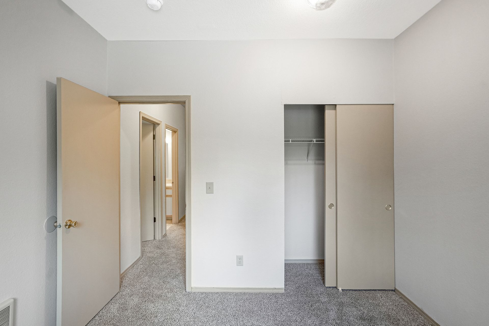 Empty white bedroom with open doors, hallway, and closet with sliding doors.