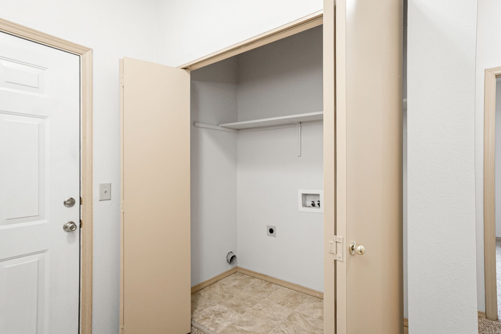 Empty beige closet with open doors and a wire shelf, next to a white interior door.
