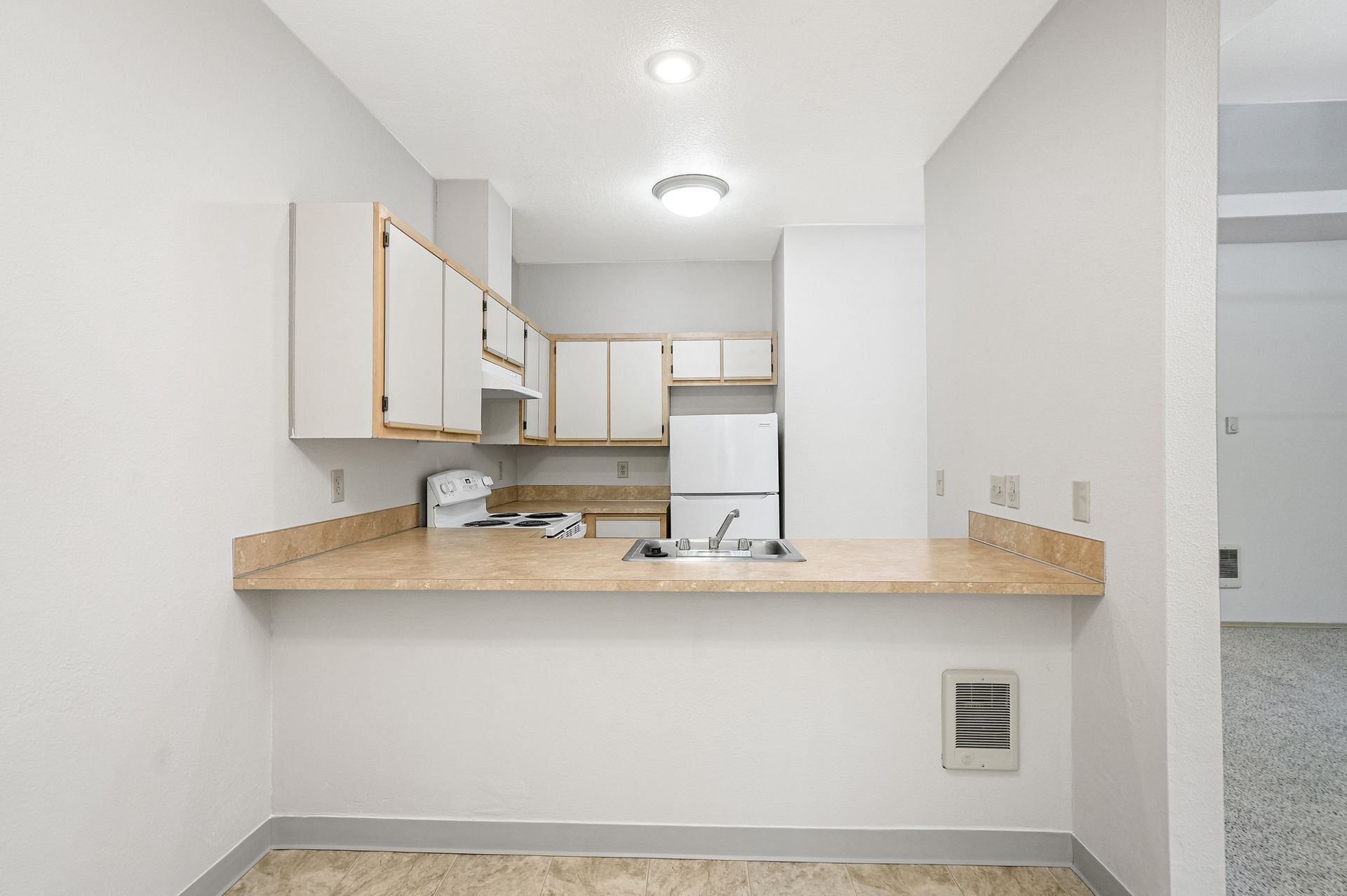 Bright white kitchen with a beige countertop, white cabinets, and a pass-through opening.