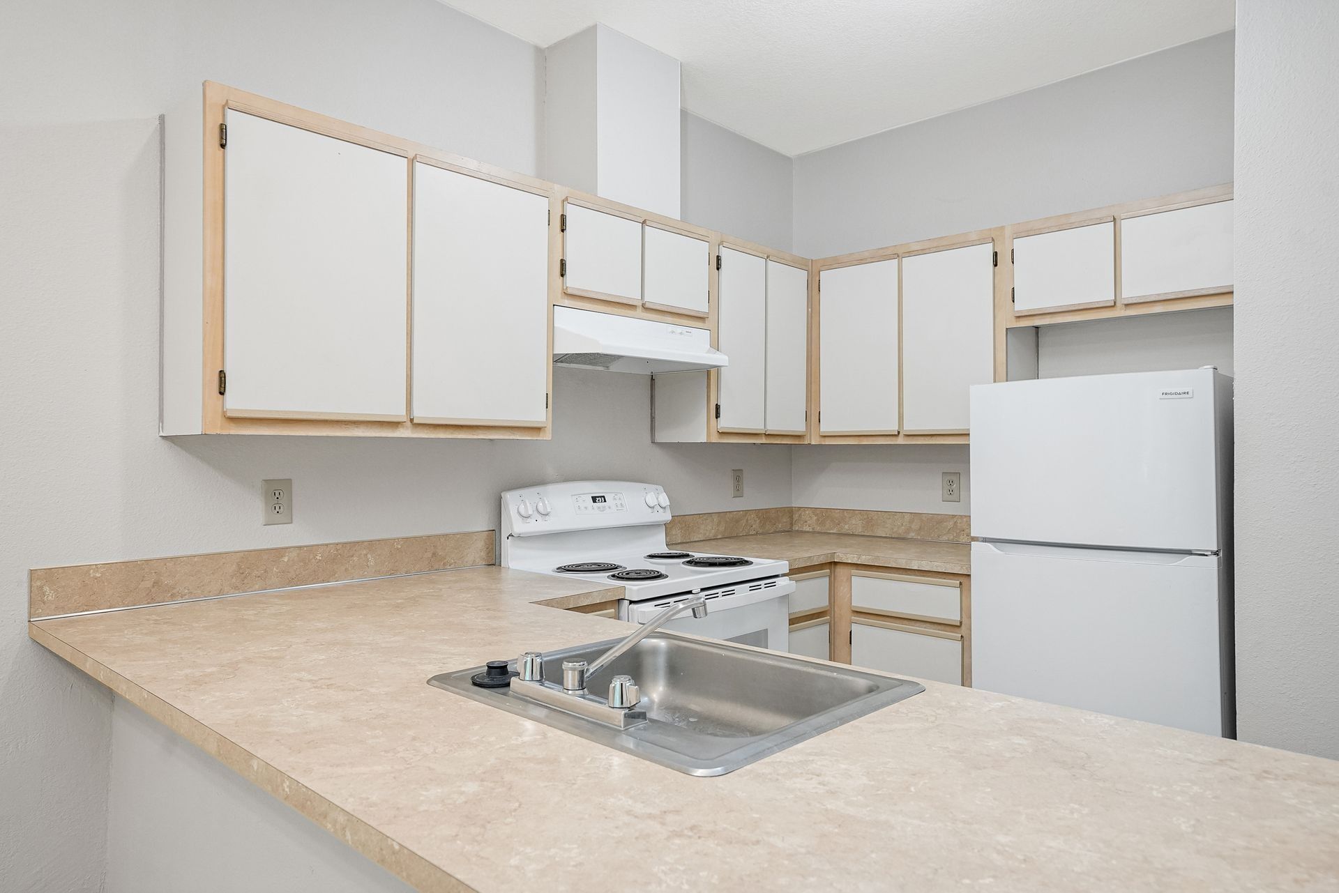 Empty beige kitchen with white cabinets, white appliances, and a central sink island