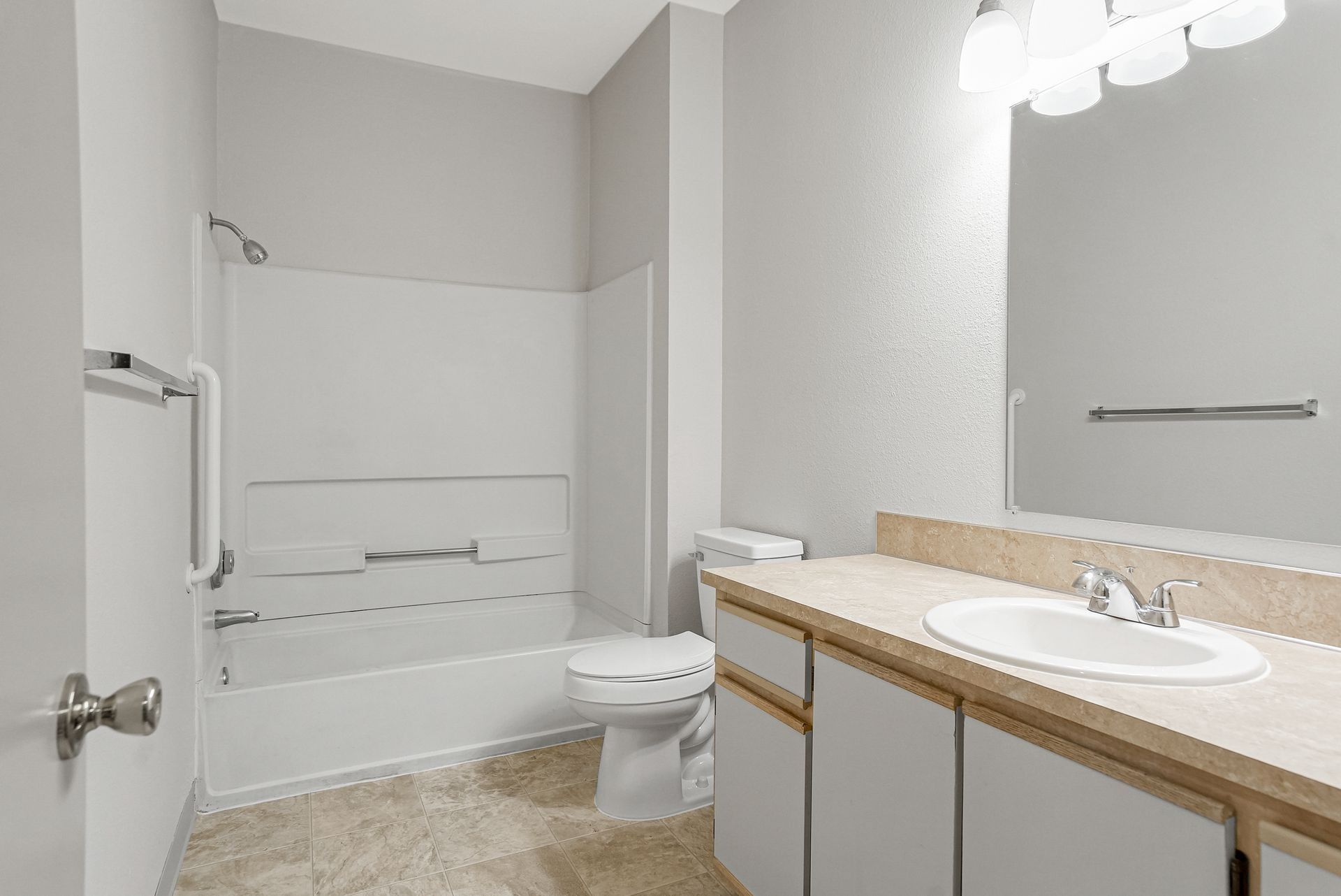 Bright accessible bathroom with walk-in shower, toilet, and vanity sink in white and beige tones