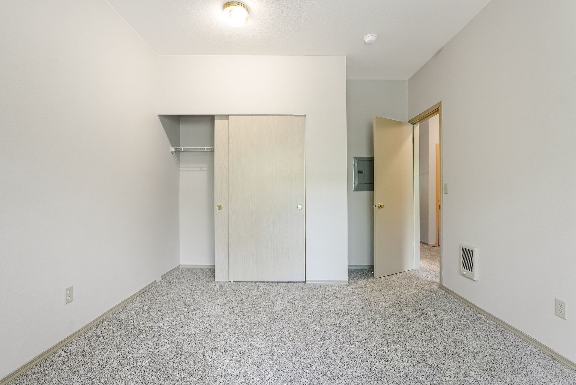 Empty white bedroom with carpeted floor, closet, and open doorway to hall