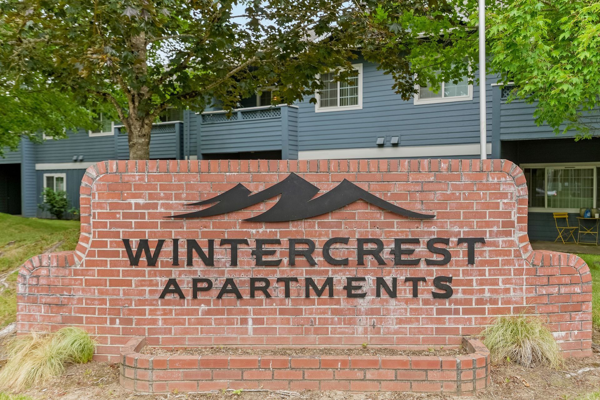 Brick entrance sign reading “Wintercrest Apartments” with trees and apartment buildings behind it