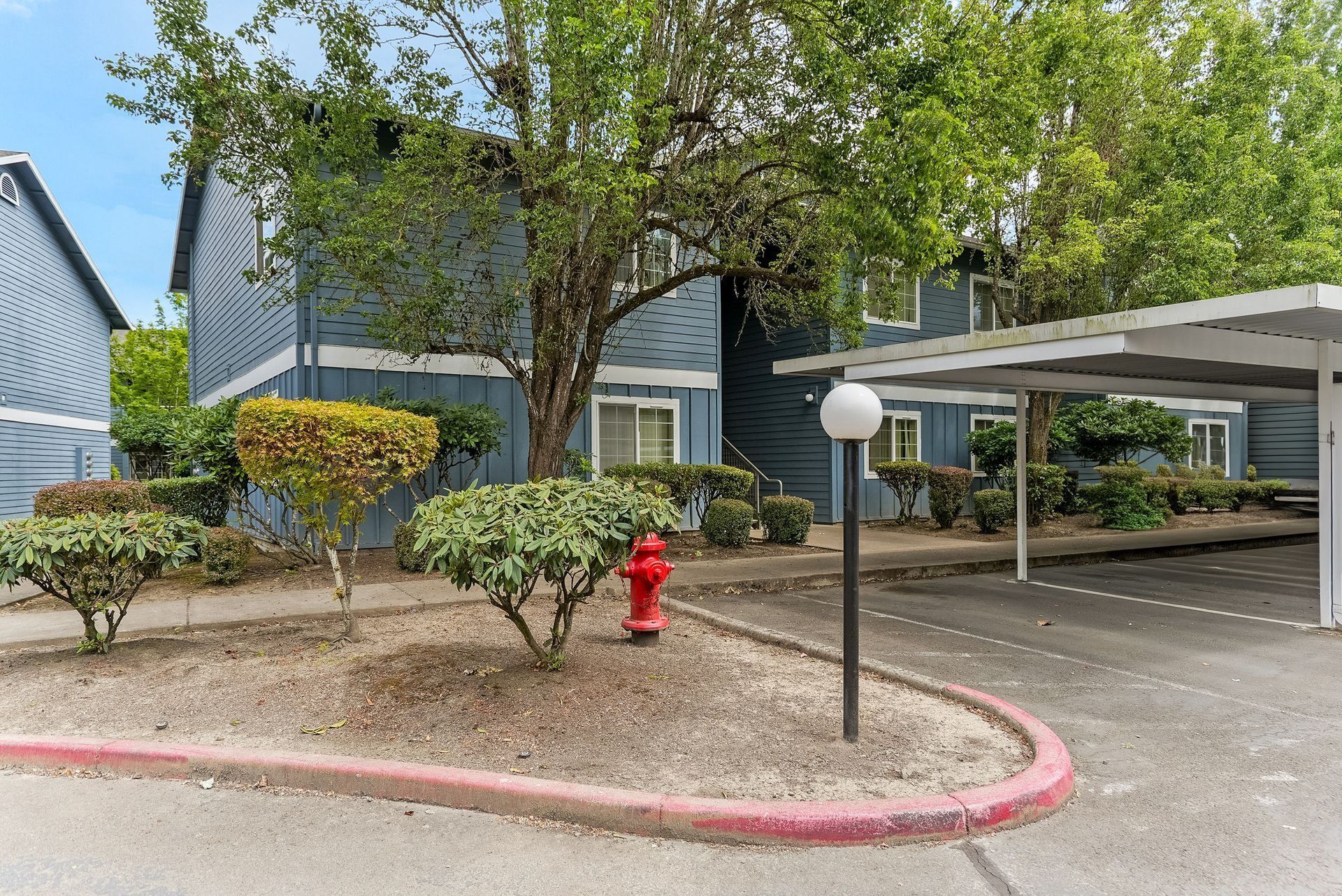 Apartment parking lot with trees, red fire hydrant, and covered carport beside a blue building.