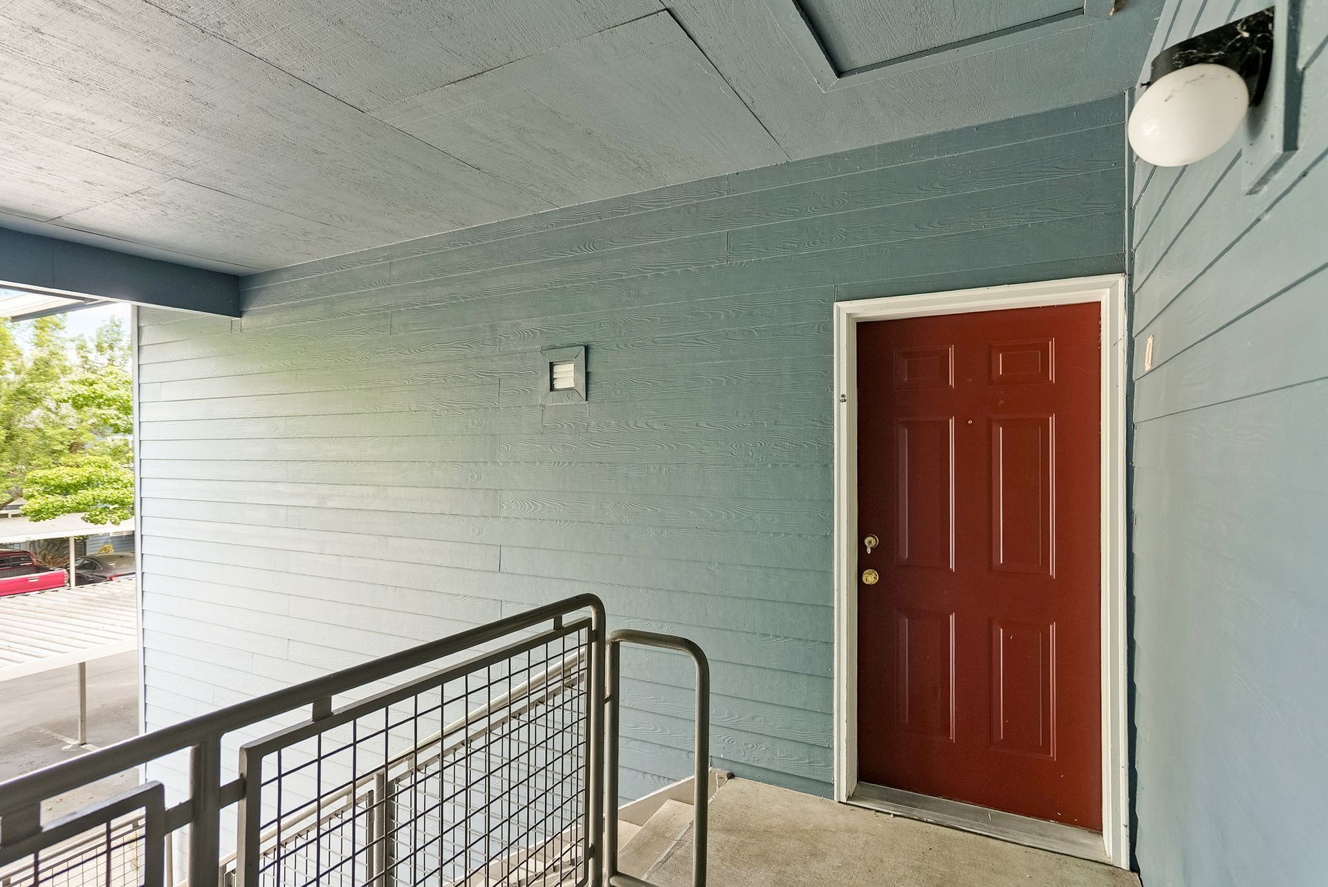 Covered apartment entryway with red door, black railing, and teal brick walls