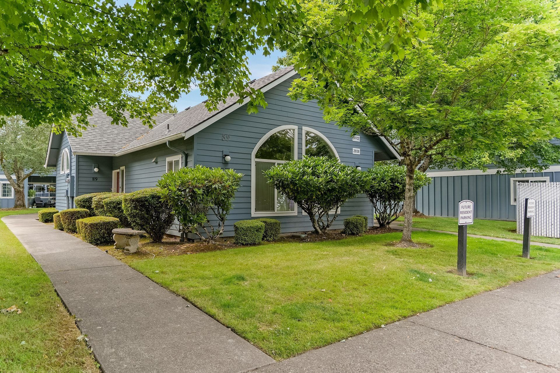 Gray house with arched window, front lawn, sidewalk, and trees on a sunny day
