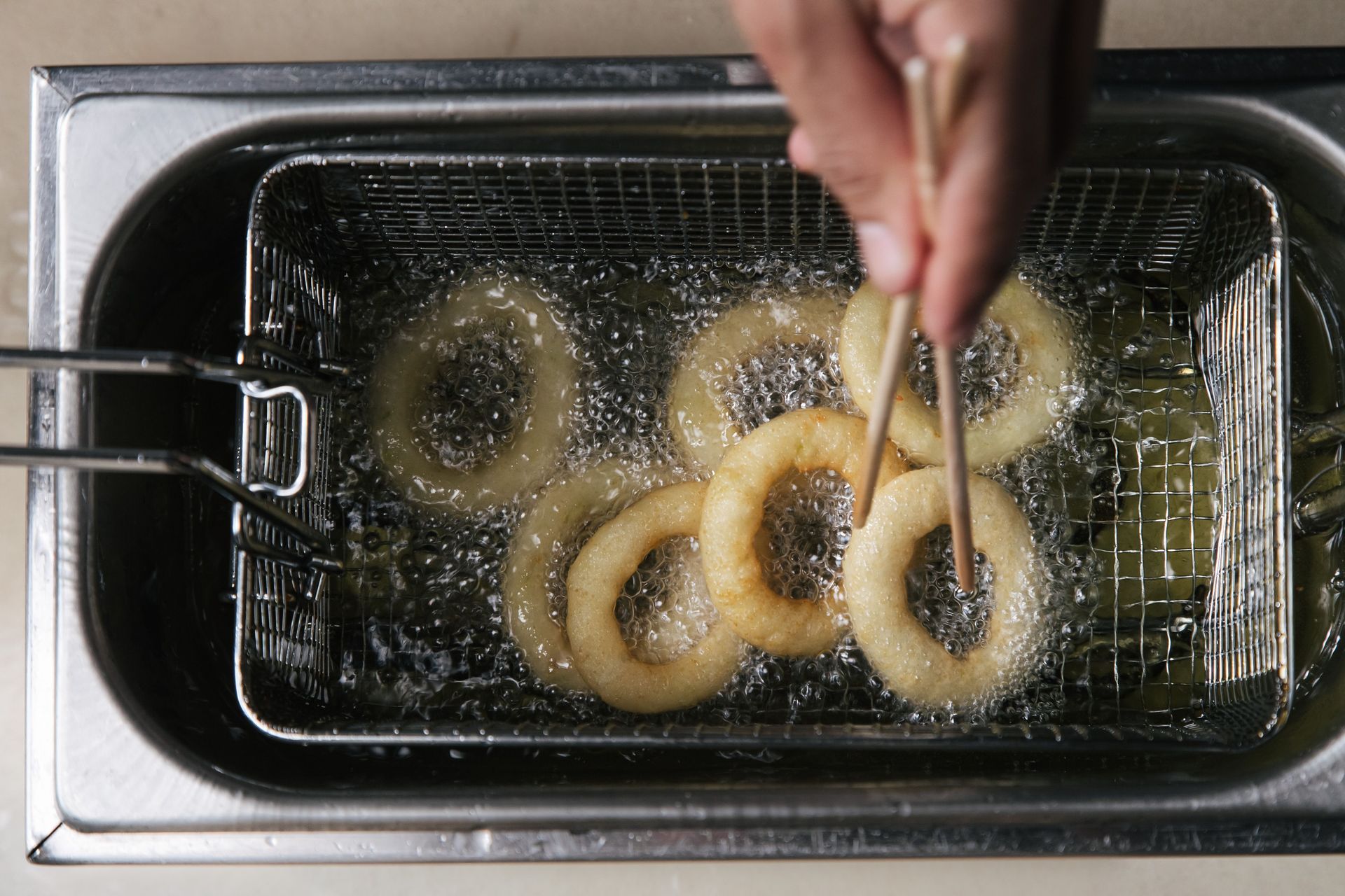 Hands lifting onion rings from a frying basket in hot oil