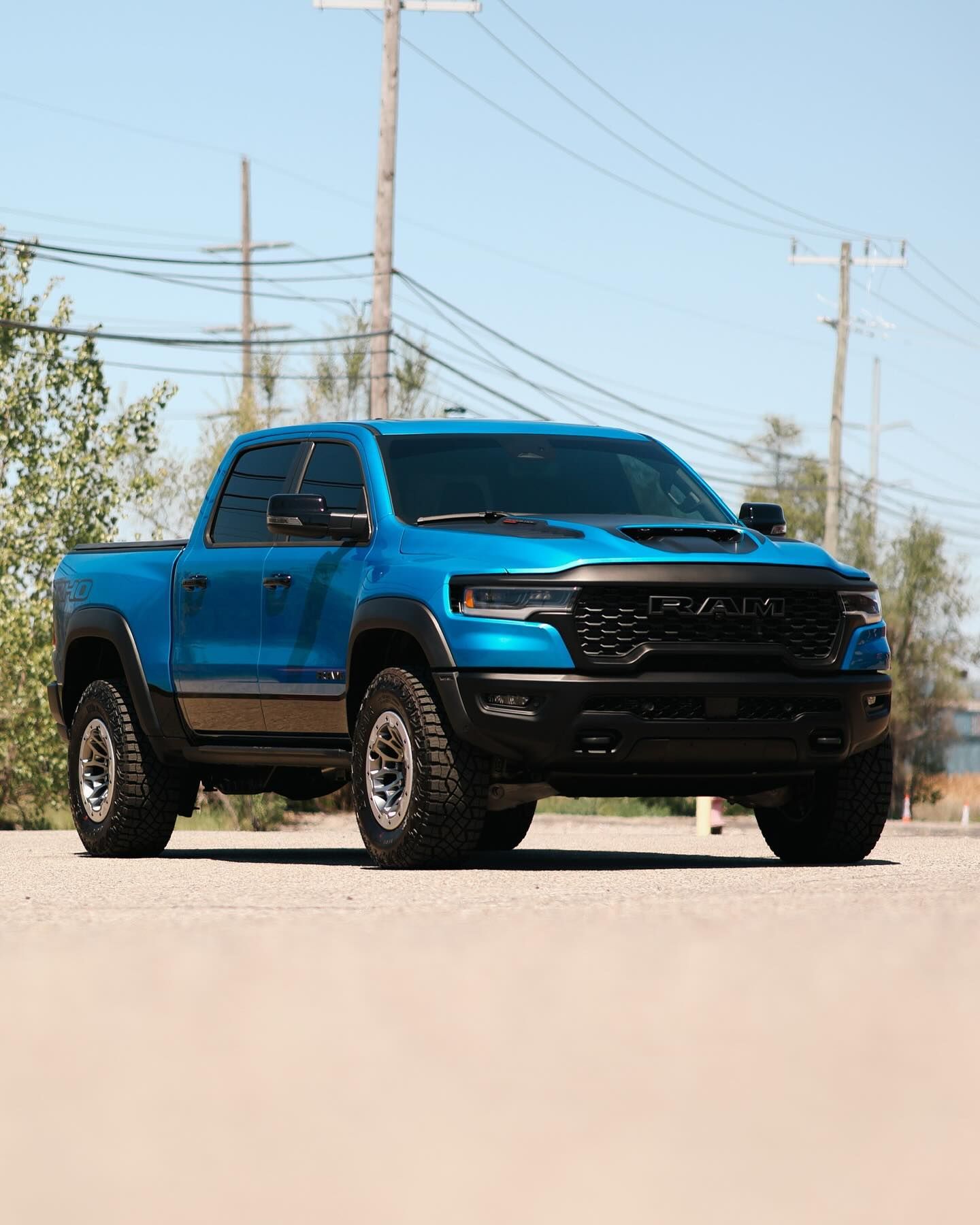 Blue pickup truck parked on a road under a clear sky, with utility poles in the background