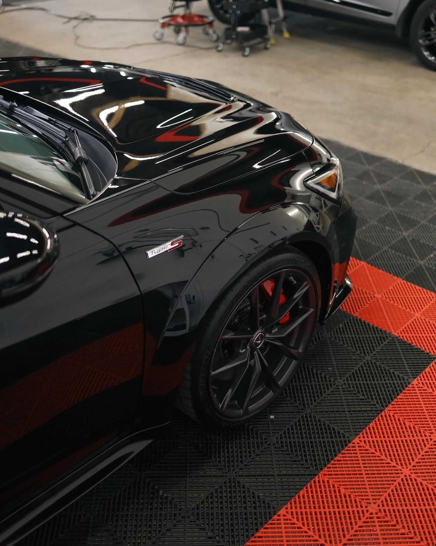 White car with gold rims on a red and black floor, against a white and black wall.