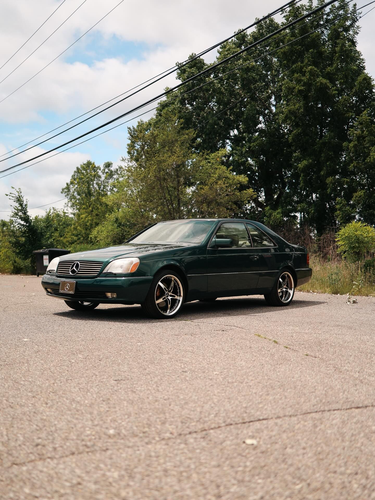 Dark green sedan parked on a roadside under trees on a sunny day