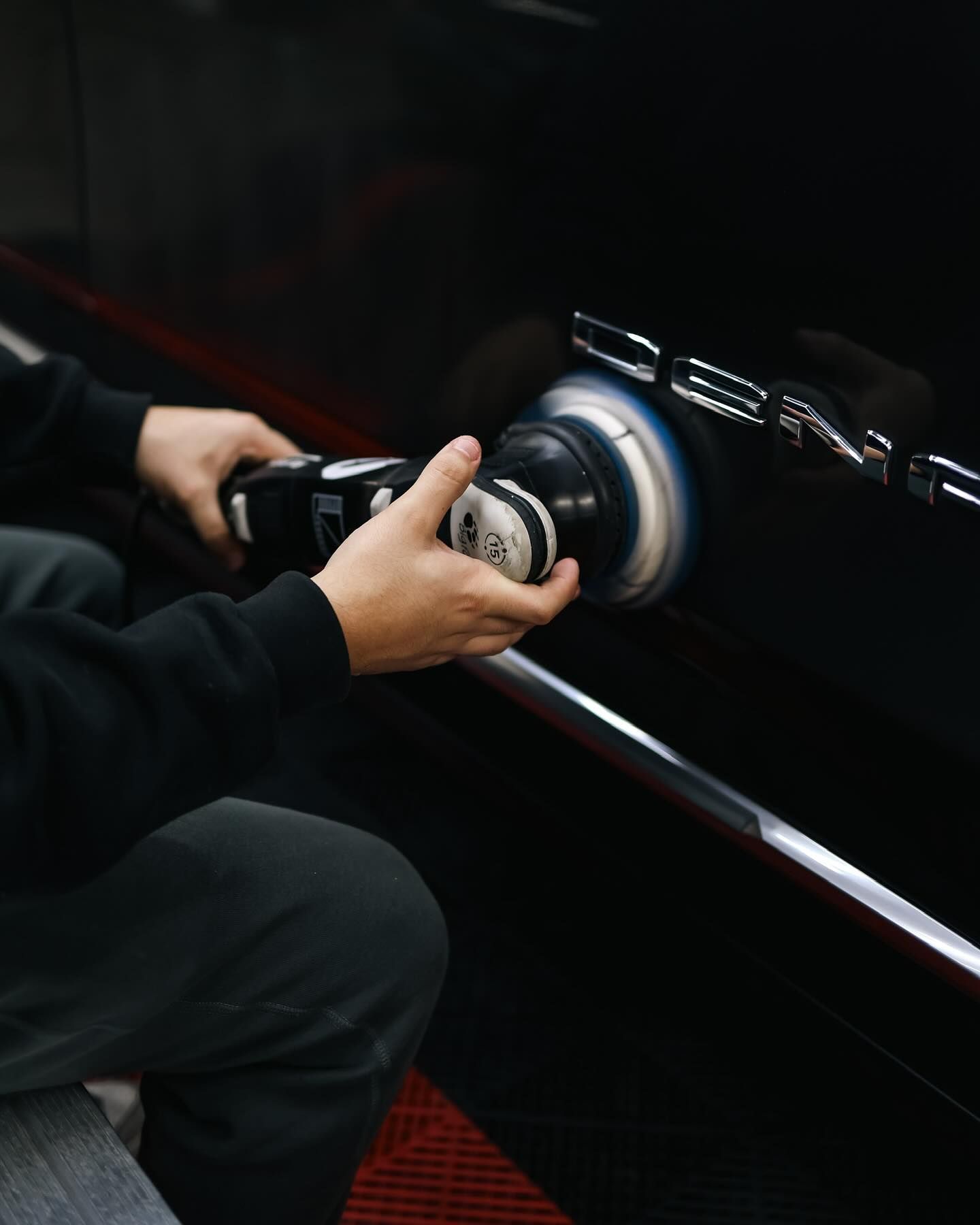 Technician performing paint correction on a black GMC vehicle with a professional polishing machine.