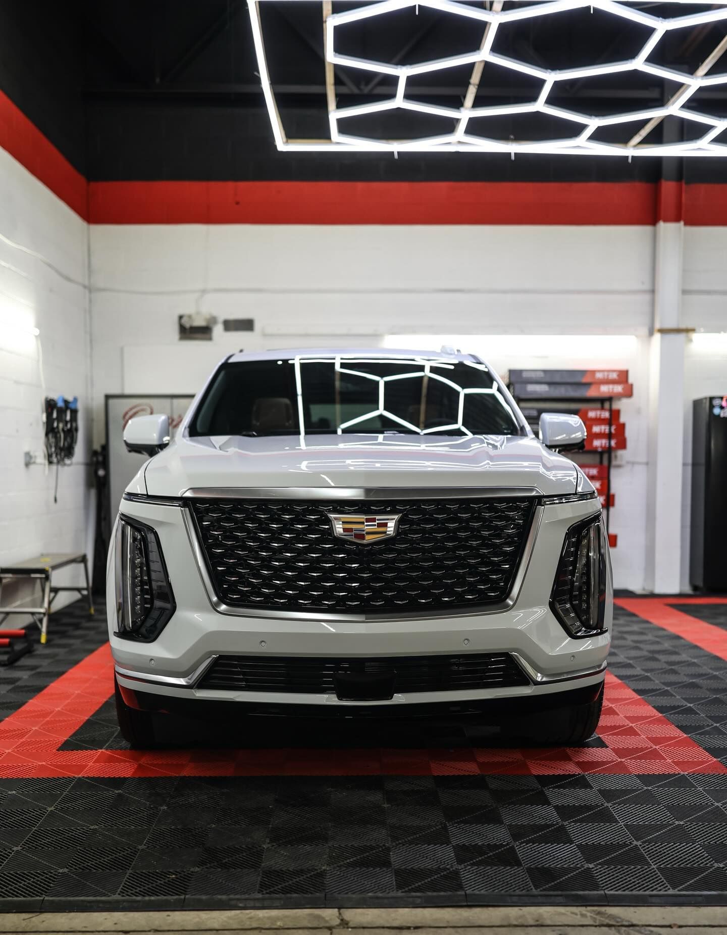 Silver Cadillac SUV parked indoors on a black-and-red checkered floor under bright ceiling lights