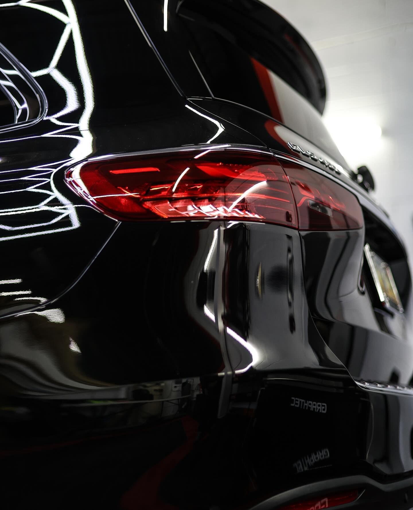 Close-up of a black car’s glossy rear with a red taillight in a showroom-like setting