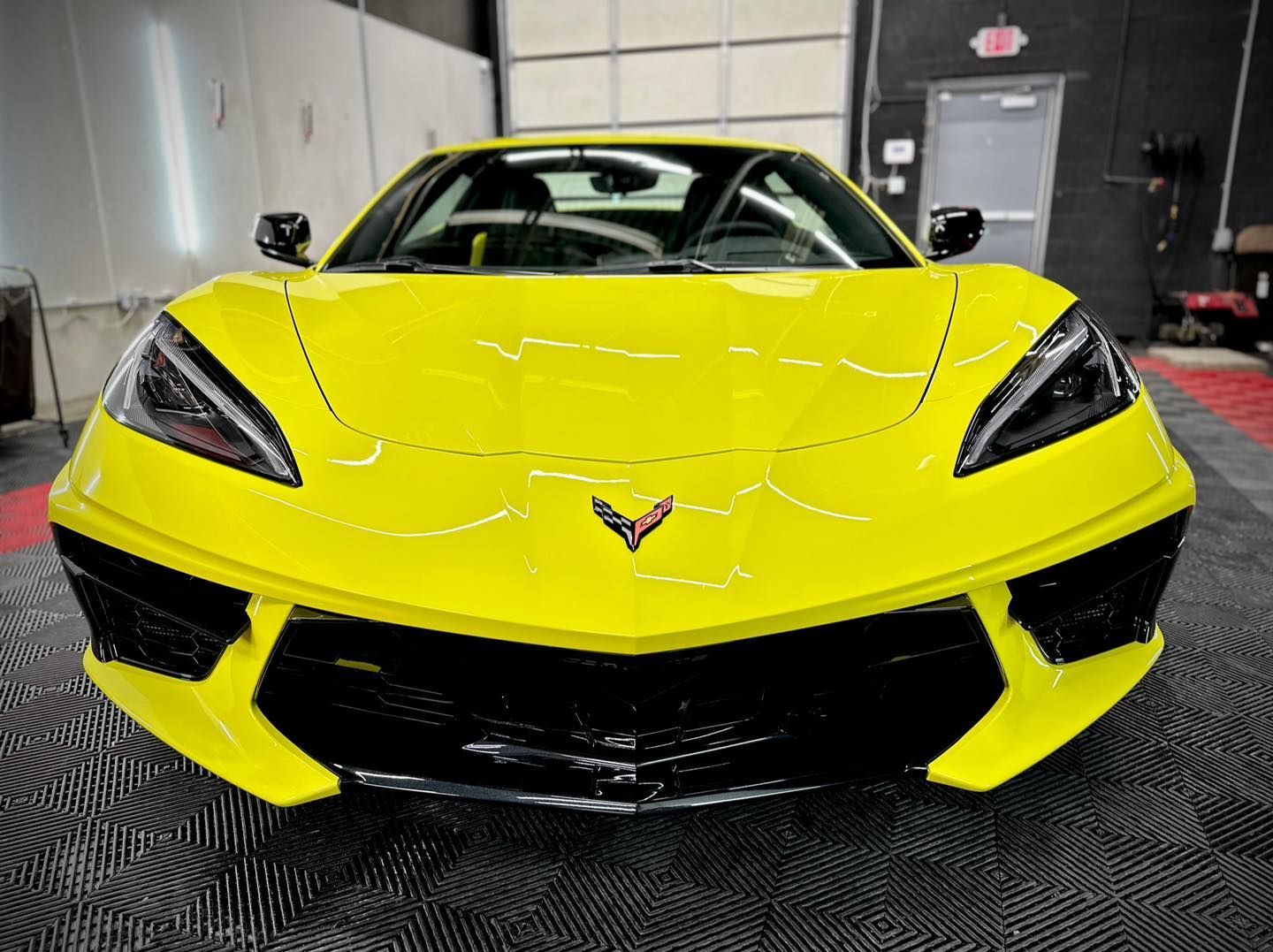 Bright yellow sports car front view in a garage, with black accents and a Corvette emblem