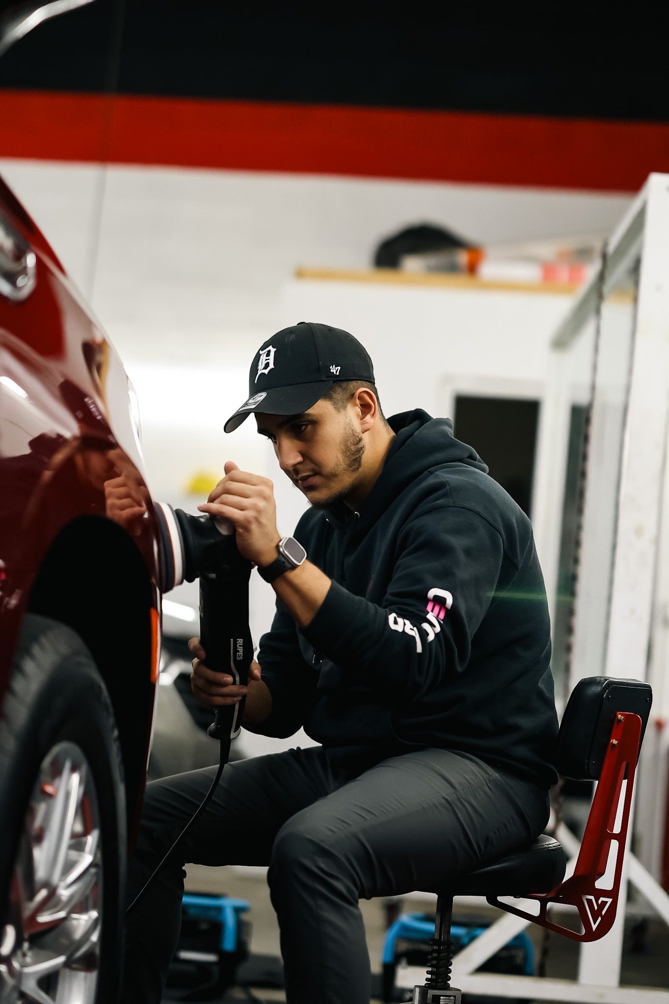 Technician performing professional paint correction on a red vehicle using a polishing machine.
